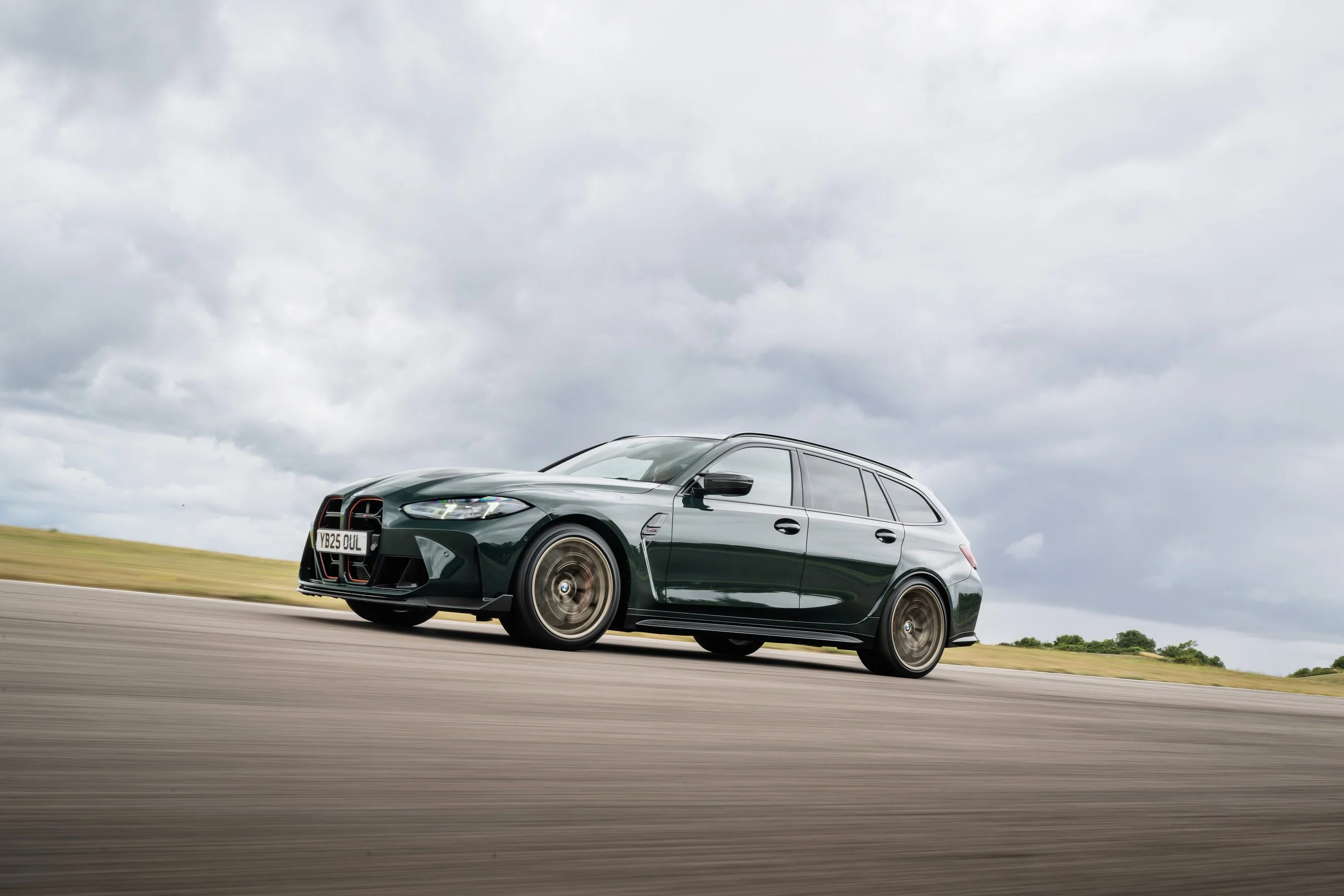 Green station wagon driving on an open road under cloudy sky.
