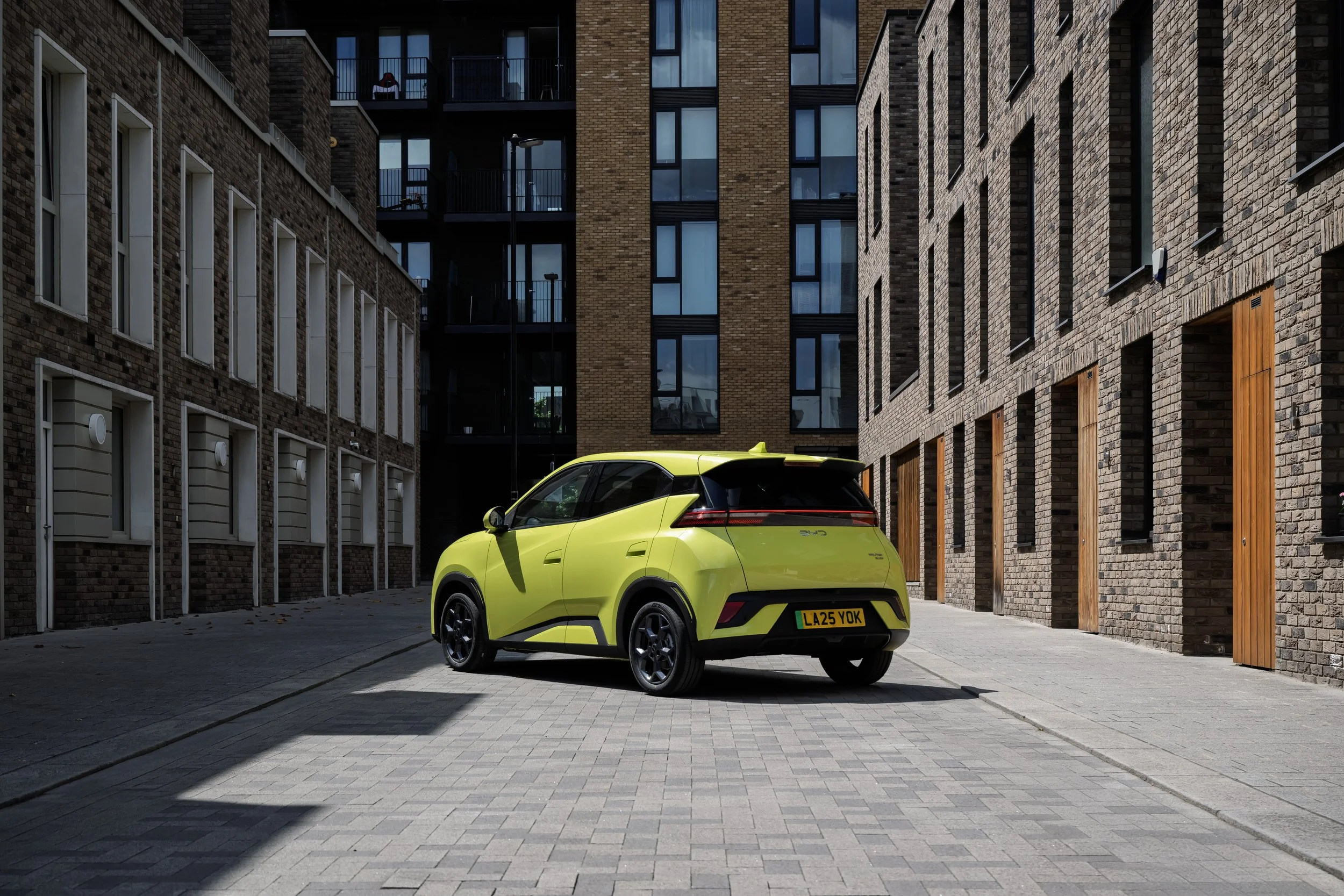 A bright yellow compact electric car parked on a modern brick city street with tall brick residential buildings in the background.