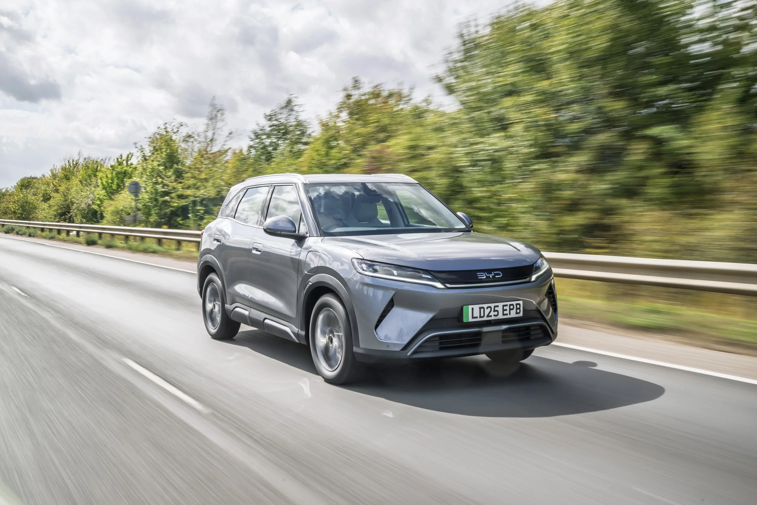 A silver electric SUV driving on a highway with blurred green trees in the background.