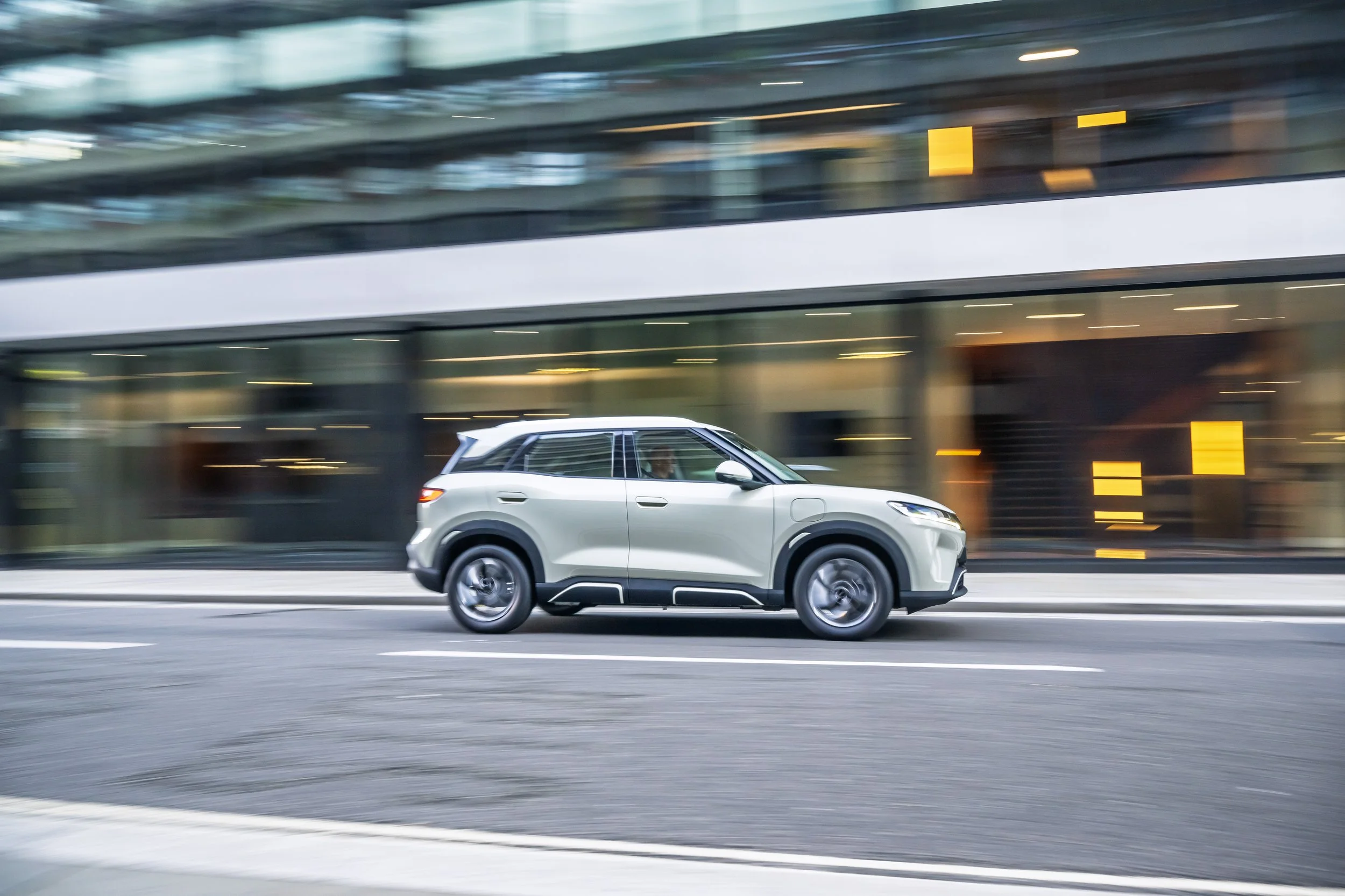 A white SUV driving quickly on a city street with modern buildings in the background, captured with motion blur.