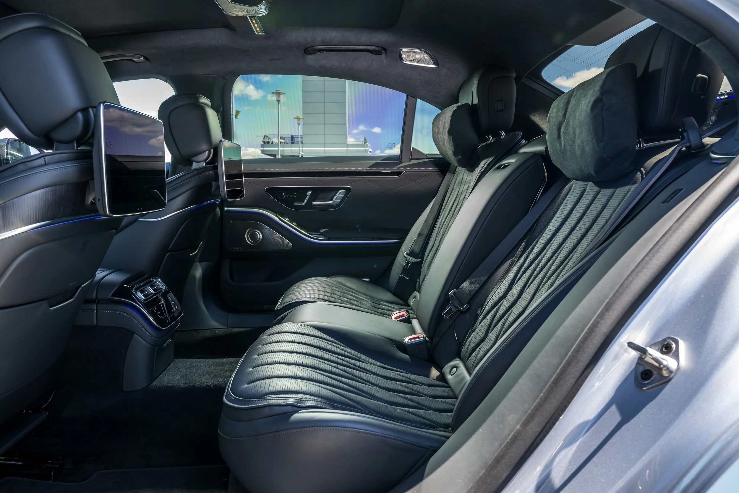 Interior of a luxury car with black leather seats, headrest pillows, rear entertainment screens, and climate control vents.