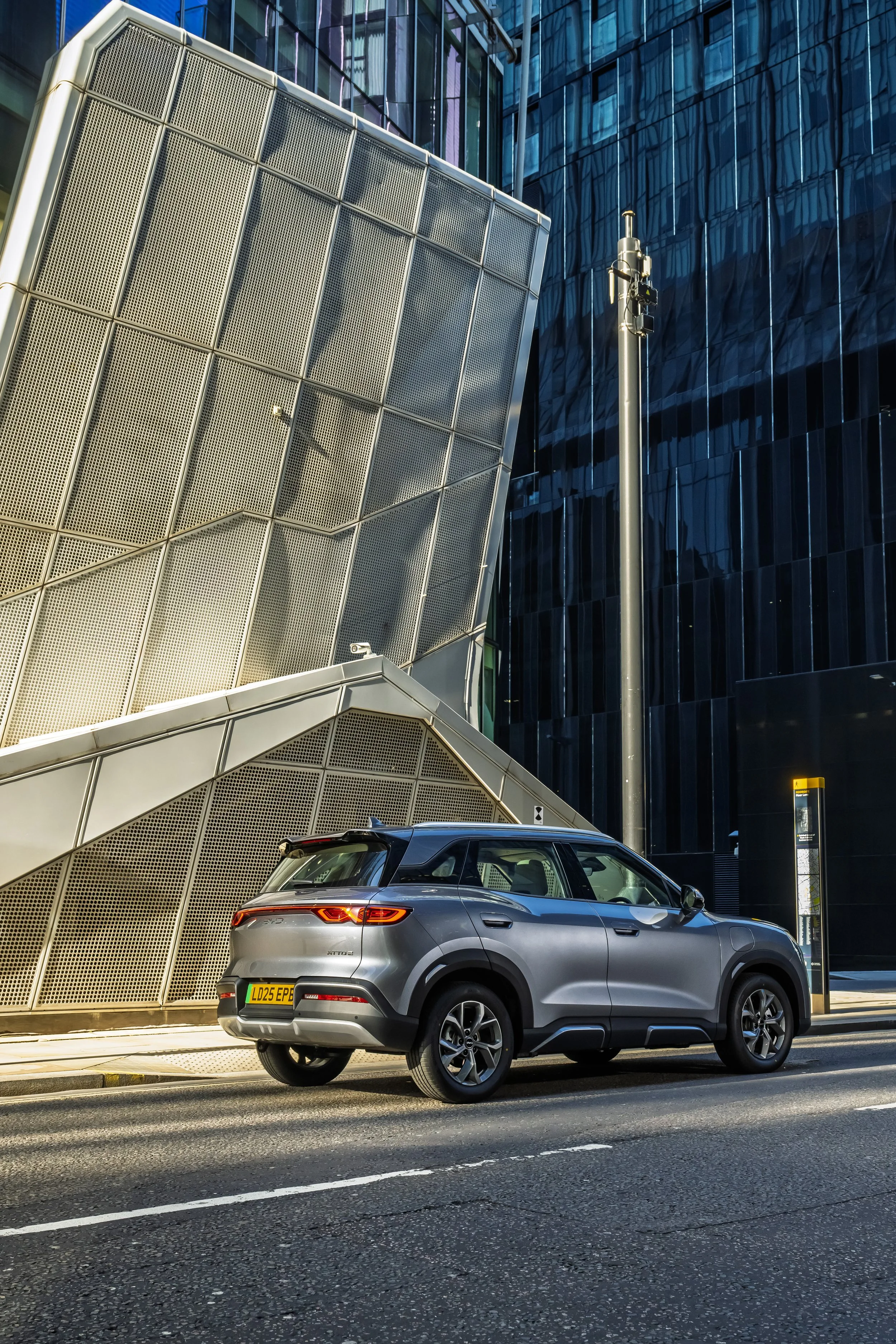 A modern silver SUV parked on a city street in front of contemporary office buildings with glass facades and geometric architecture.