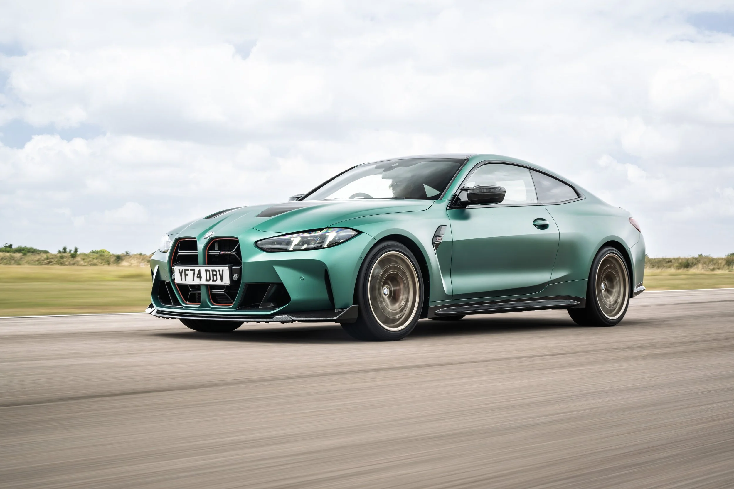 Green sports car driving on a highway with a cloudy sky in the background.