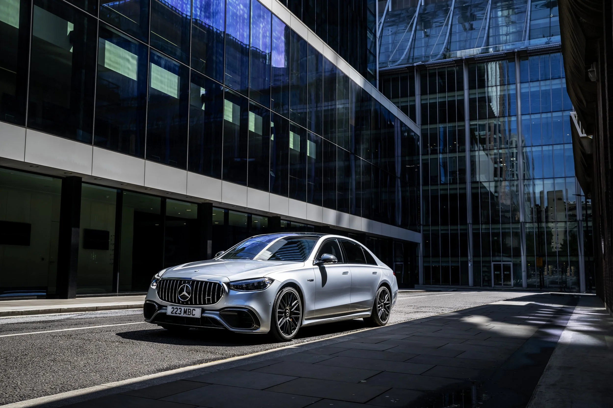 A silver Mercedes-Benz parked on a city street in front of a modern glass building.