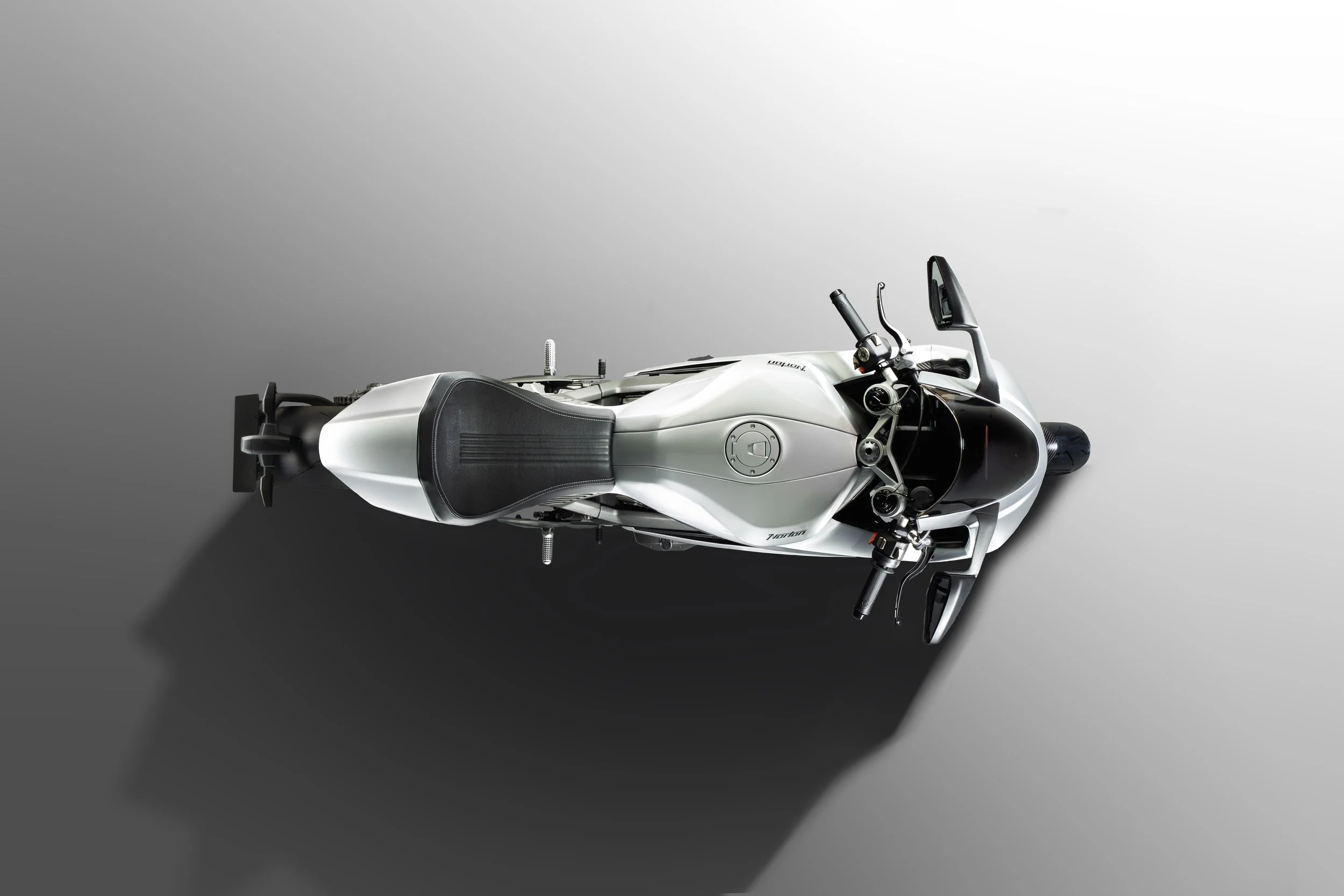 Top view of a sleek, silver sport motorcycle with black accents on a two-tone gray background, casting a shadow.