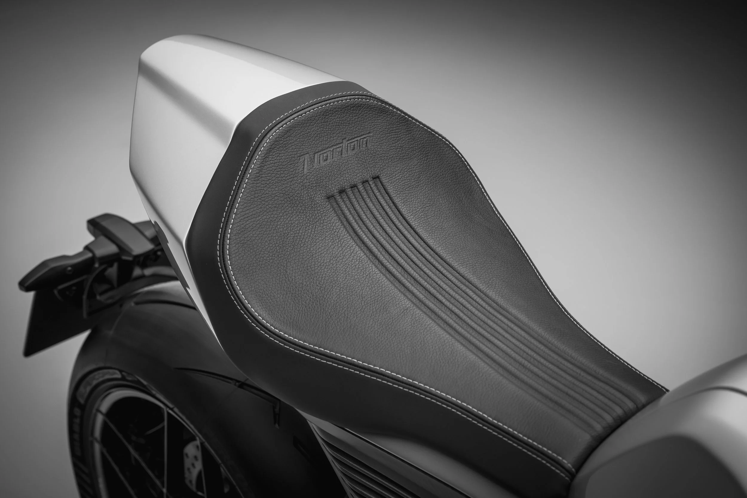 Close-up of a sleek black leather motorcycle seat with white stitching, bearing the brand name Norton.