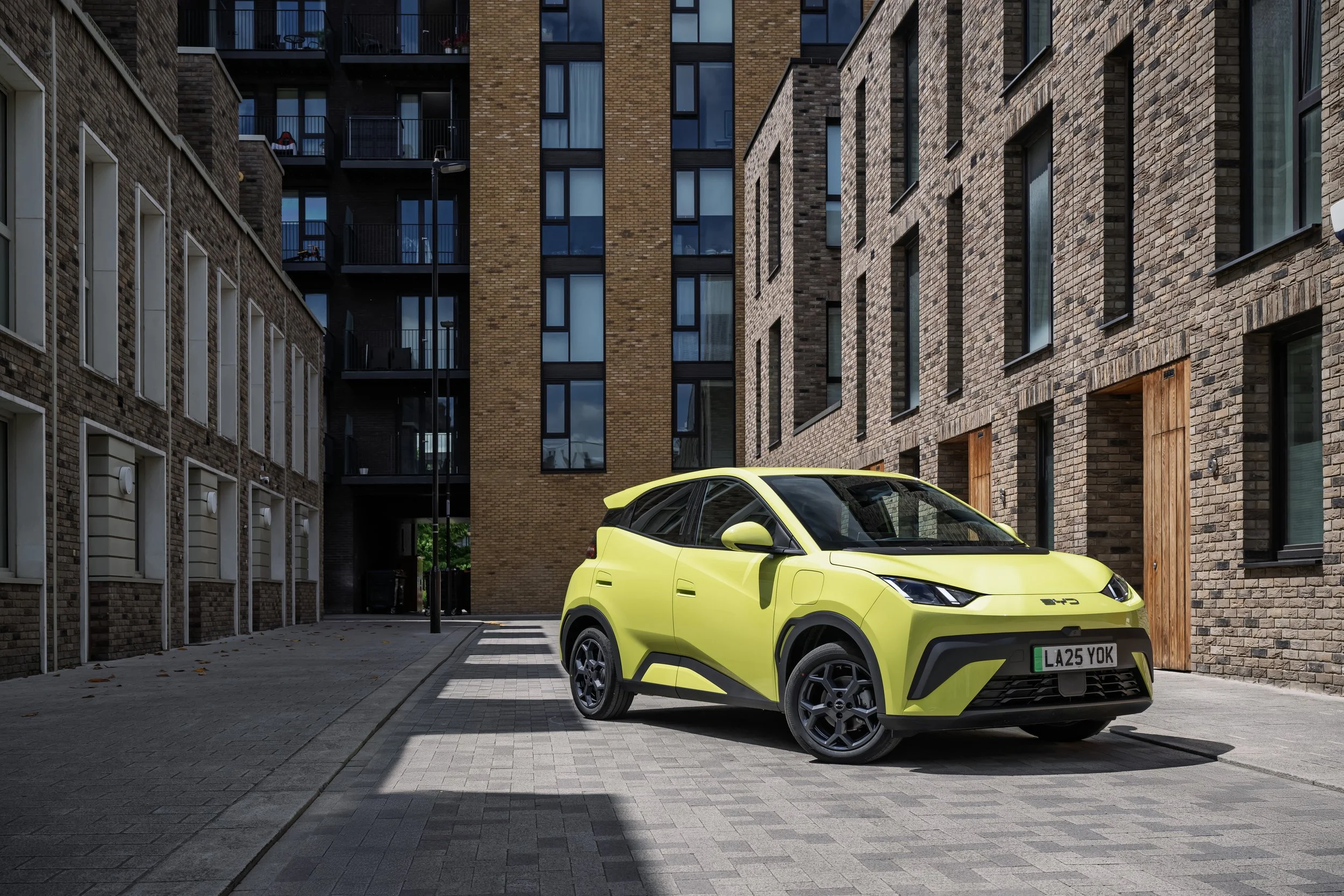 A yellow electric car parked on a paved street between modern brick apartment buildings.