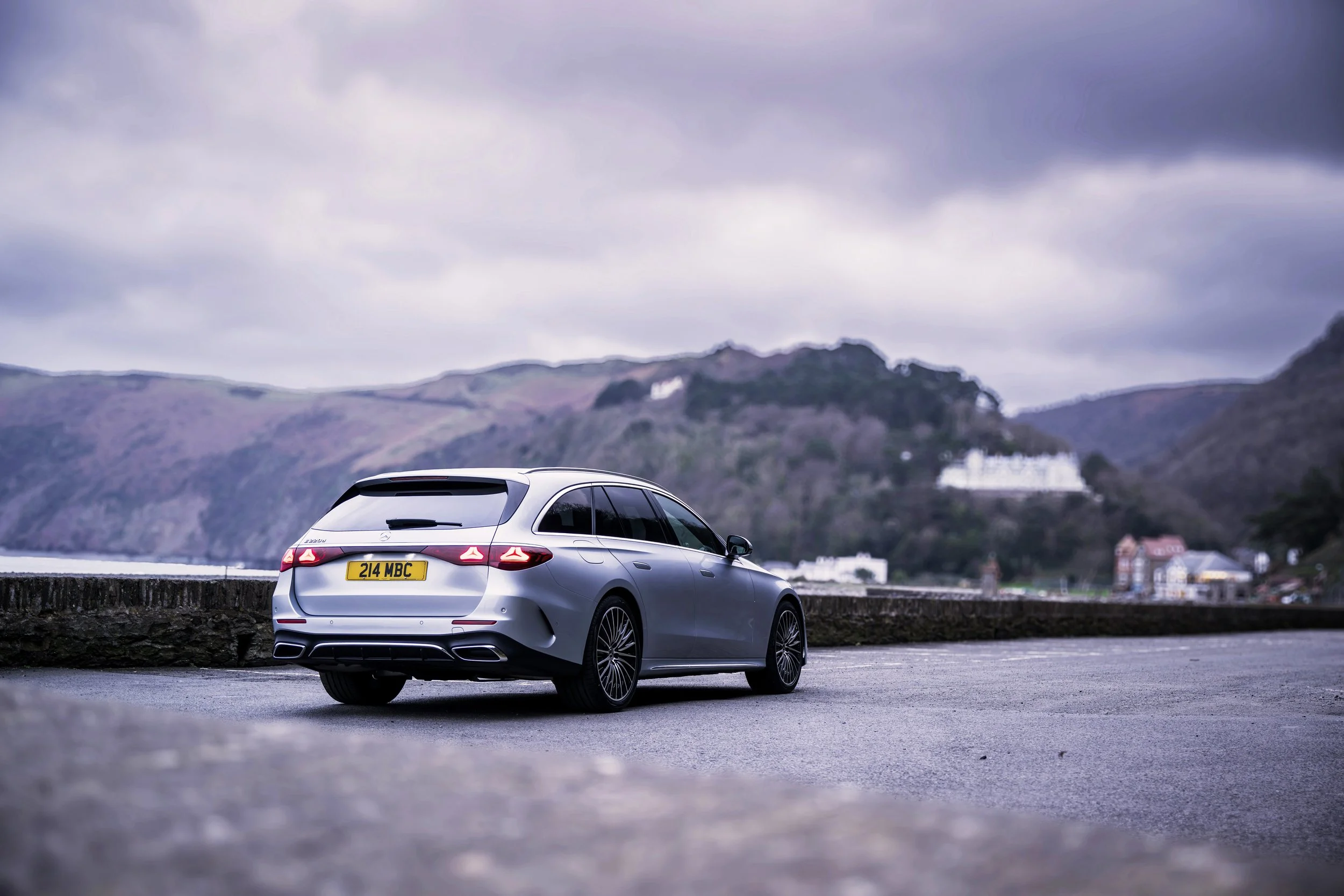 Silver station wagon car parked along a roadside with hills and cloudy sky in the background.