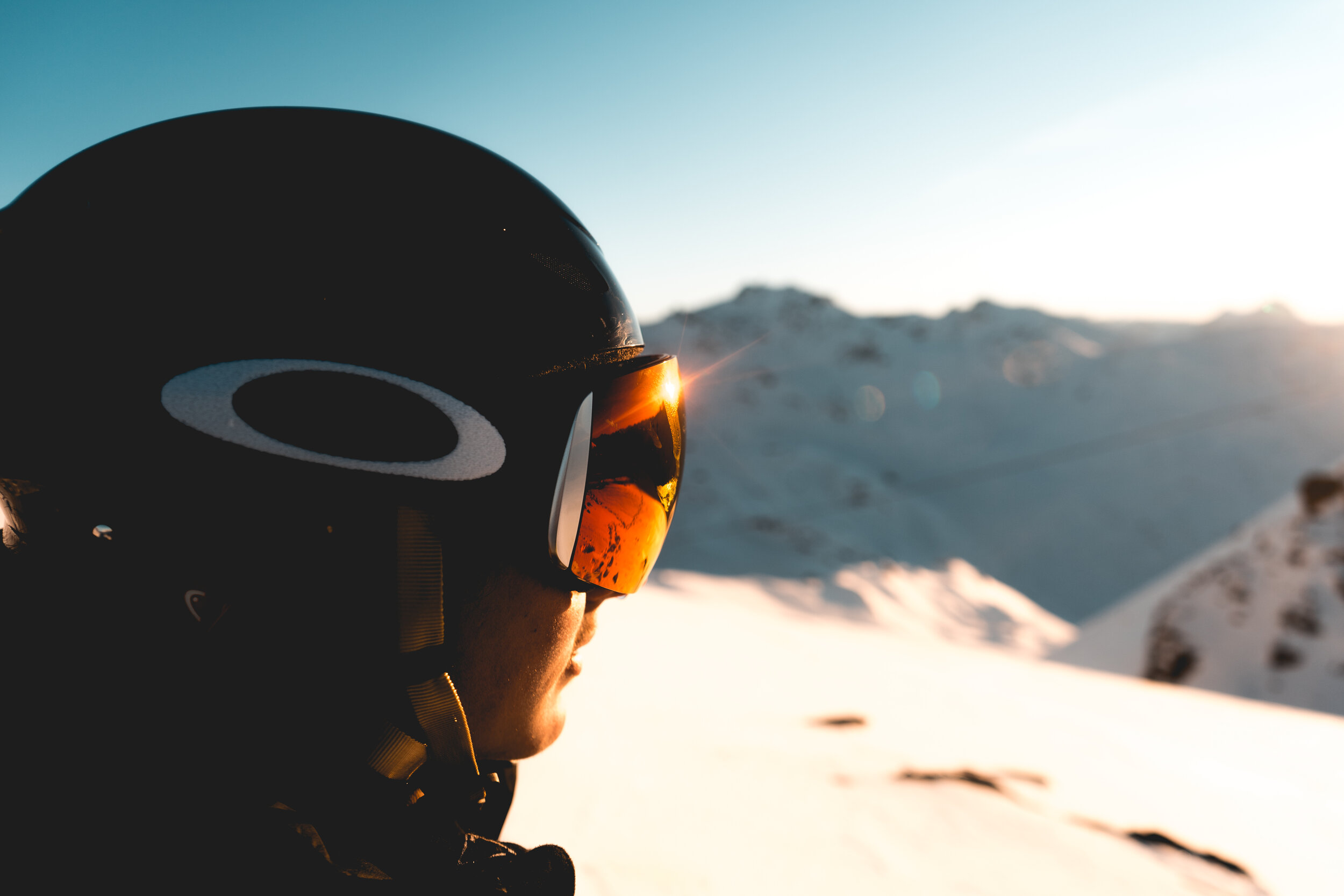 Skier wearing a helmet and goggles in snowy mountains at sunrise.