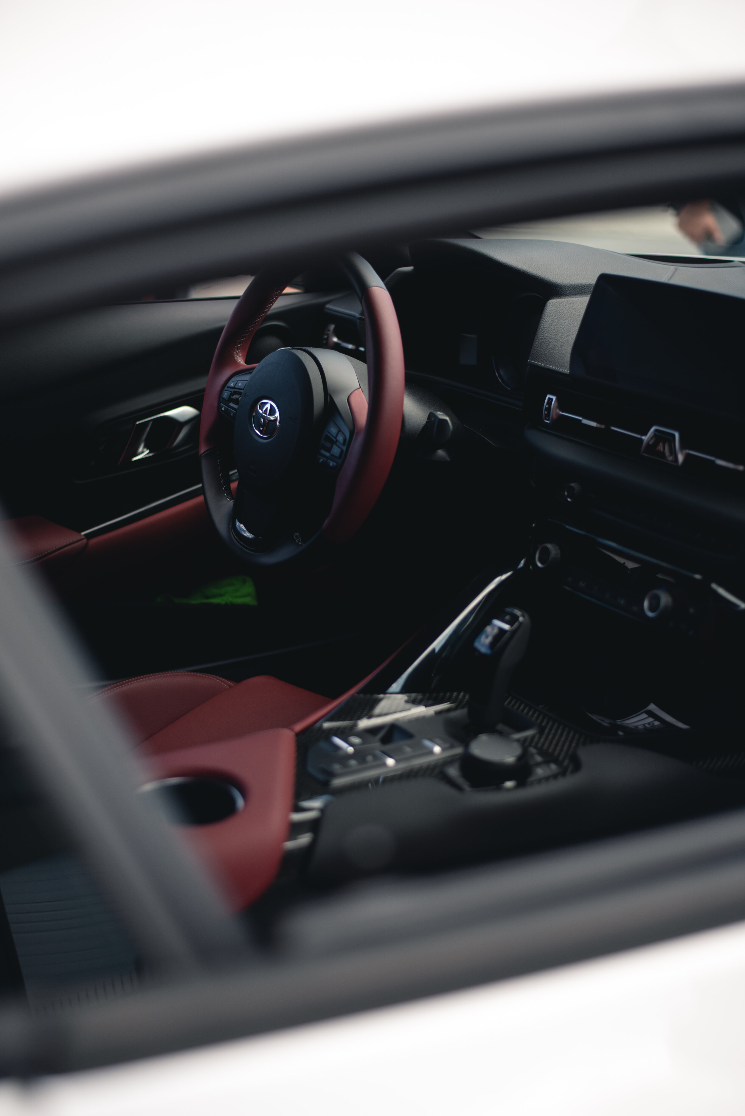 Interior of a Toyota with red and black accents, featuring the steering wheel, dashboard, and gear shift.