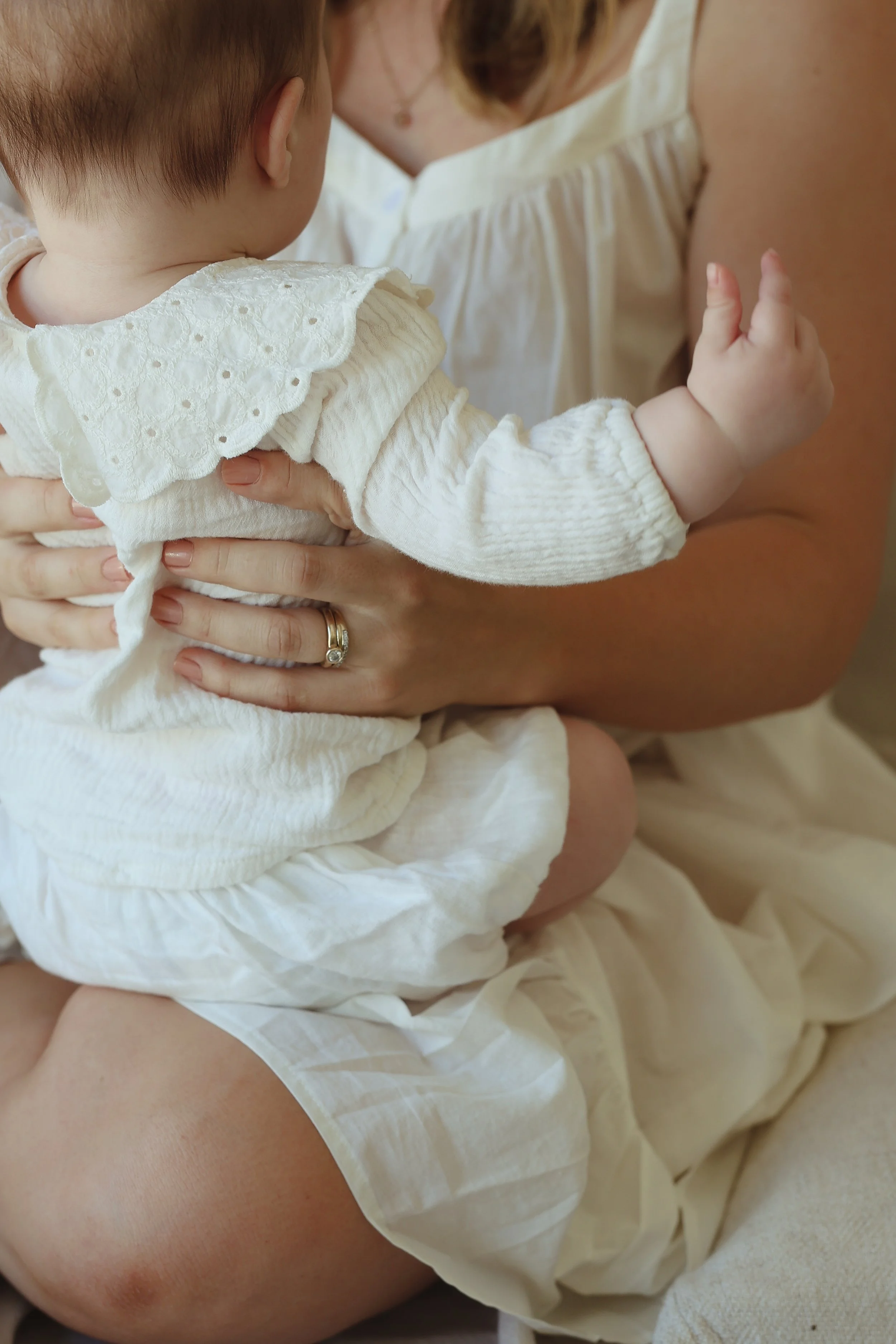 A toddler being held and breastfed by an adult woman, with the woman gently supporting the child with one hand and holding her close.