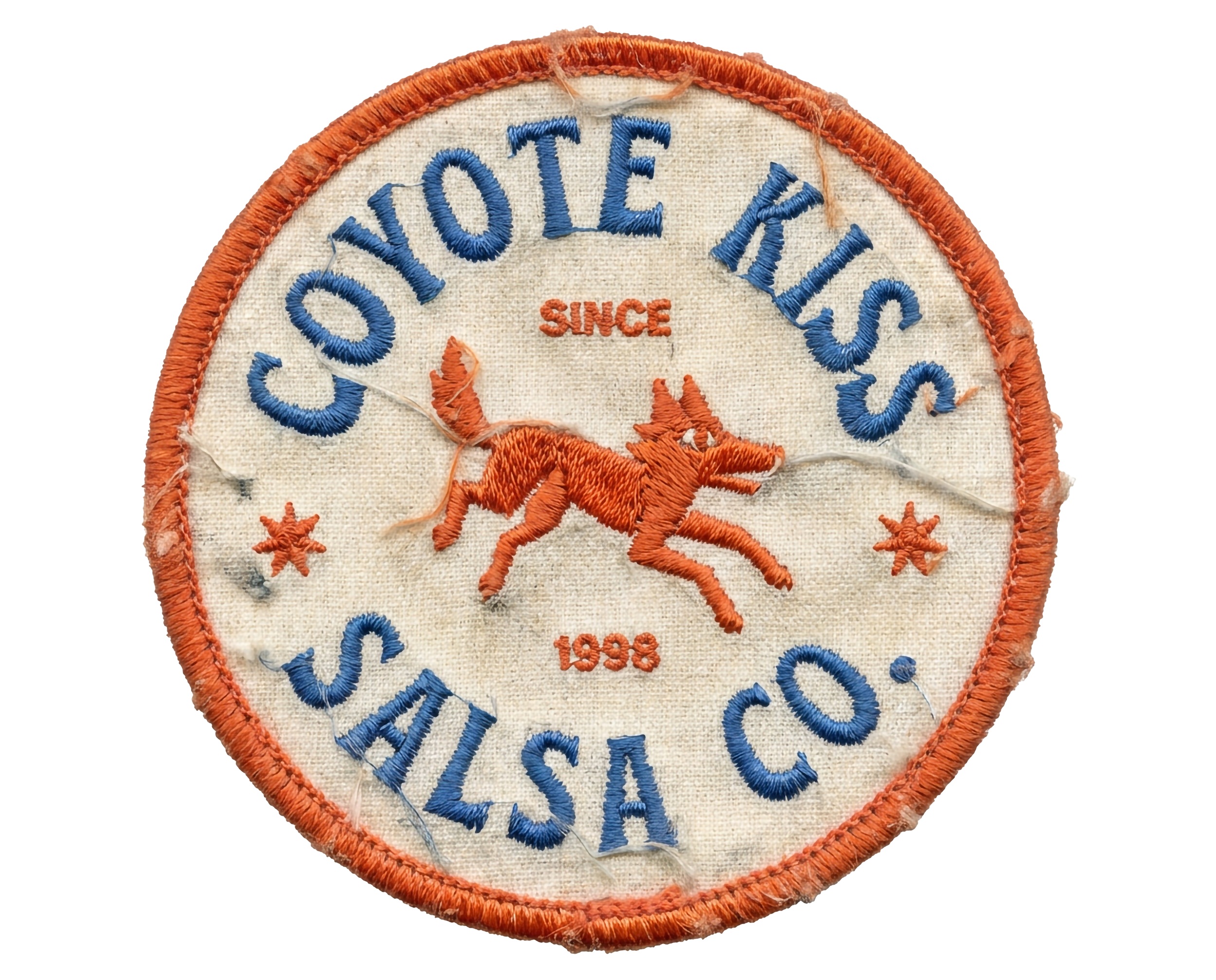 An embroidered patch with orange border, blue text reading 'Coyote K9s,' a red embroidered coyote in the center, and the words 'Since 1998' beneath the coyote. The background fabric appears off-white.