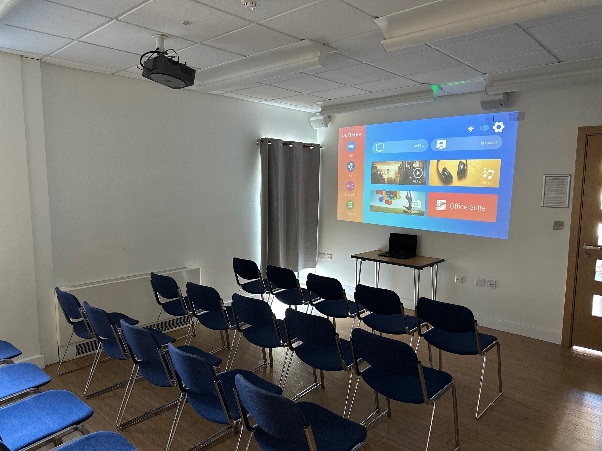 a room filled with chairs, laptop and a turned on projector.