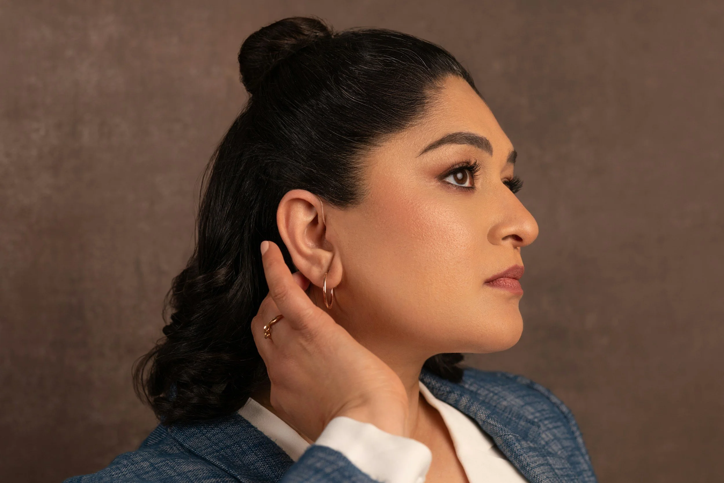 Woman with dark hair shows hearing aid by pushing hair behind ear