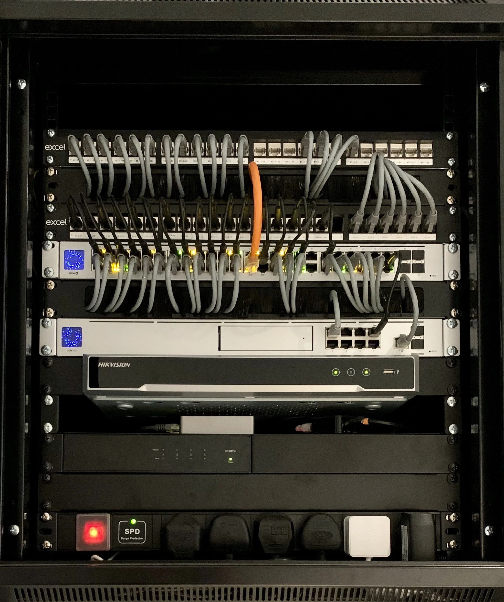Server rack with various networking and power equipment, including switches, a Hikvision device, and surge protectors.