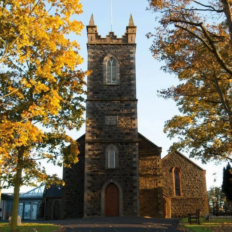 Grey stone church building with yellow autumnal tree in foreground