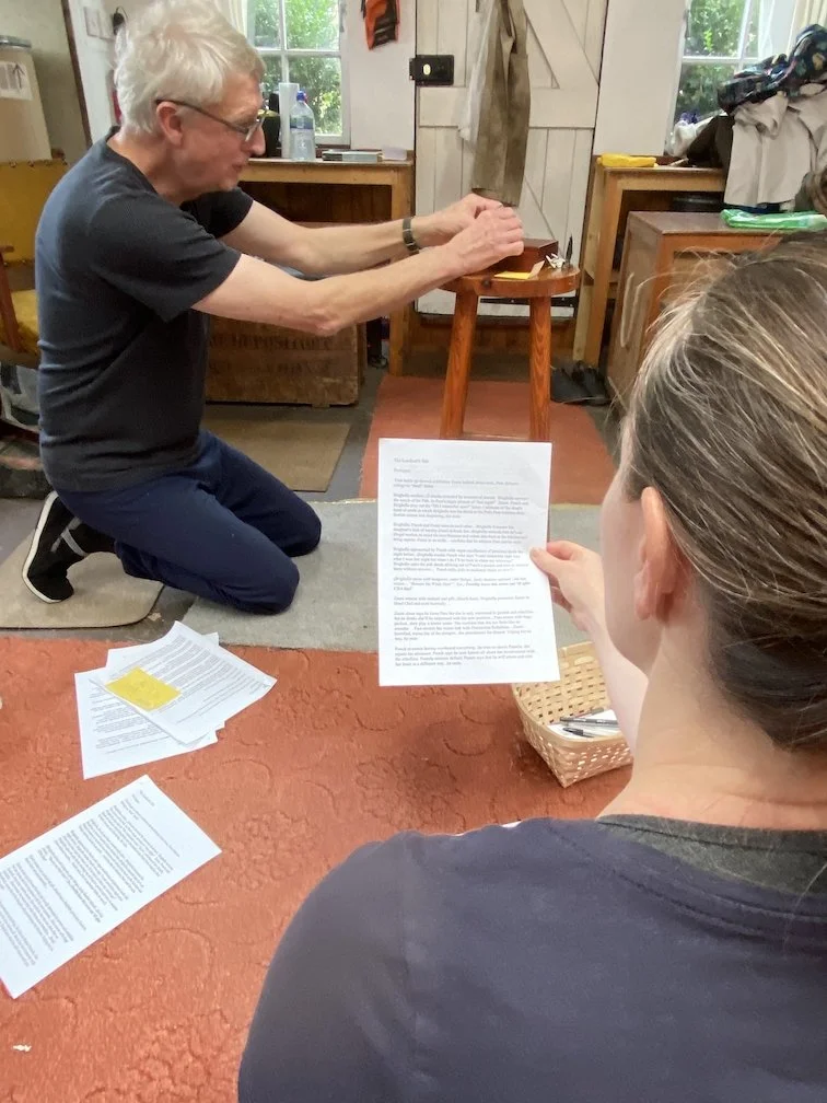 two actors, one reading from a sheet, one moving chess-like pieces on a tiny stage