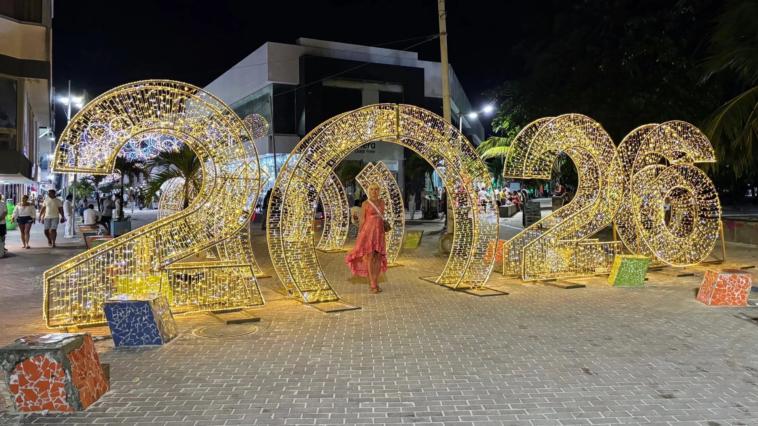 Anita in a pink dress standing among illuminated festive lights on numbers "2026" in San Andres Colombia