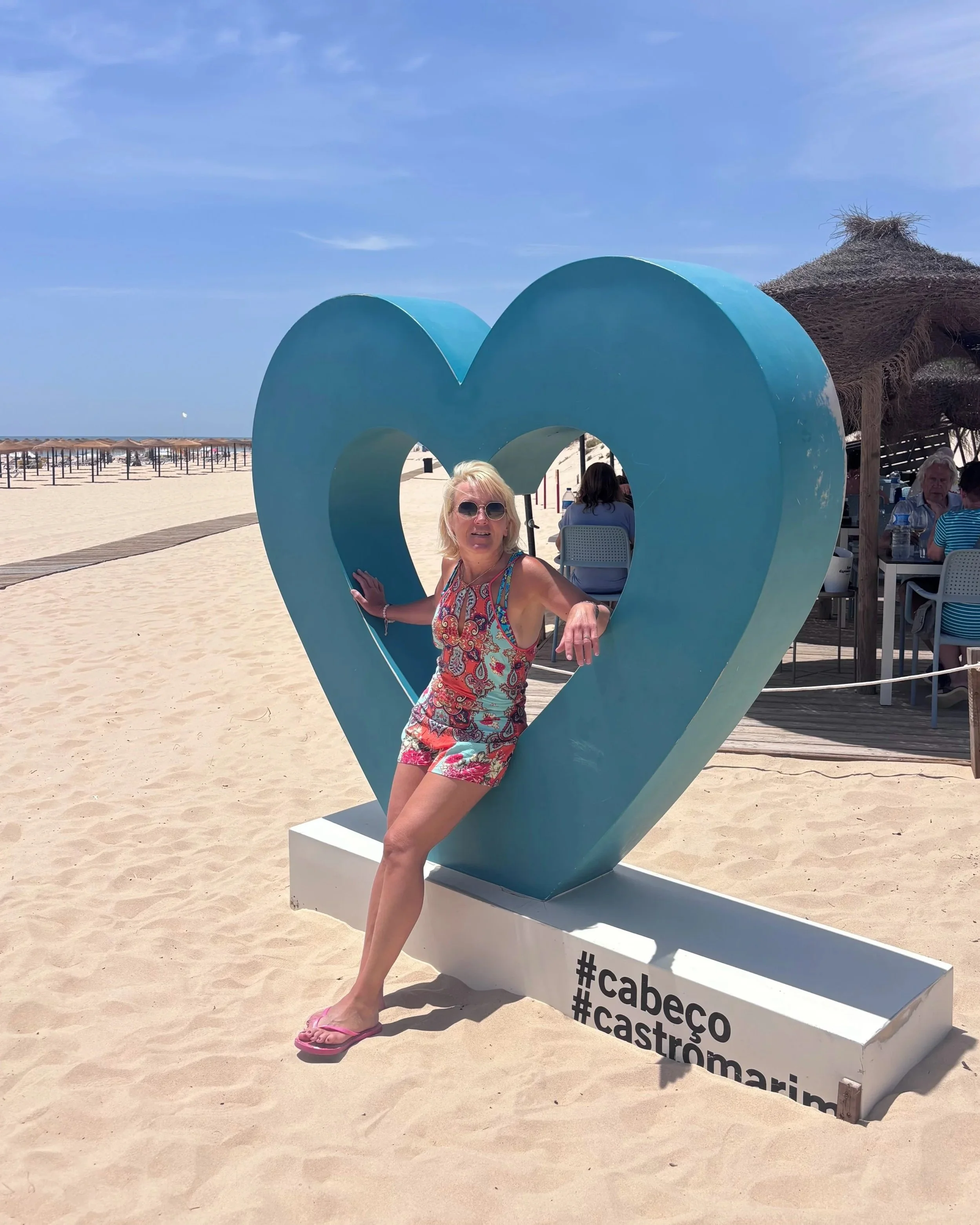 Anita inside a green heart installation on the white sand of Cabeco Beach Castro Marim.