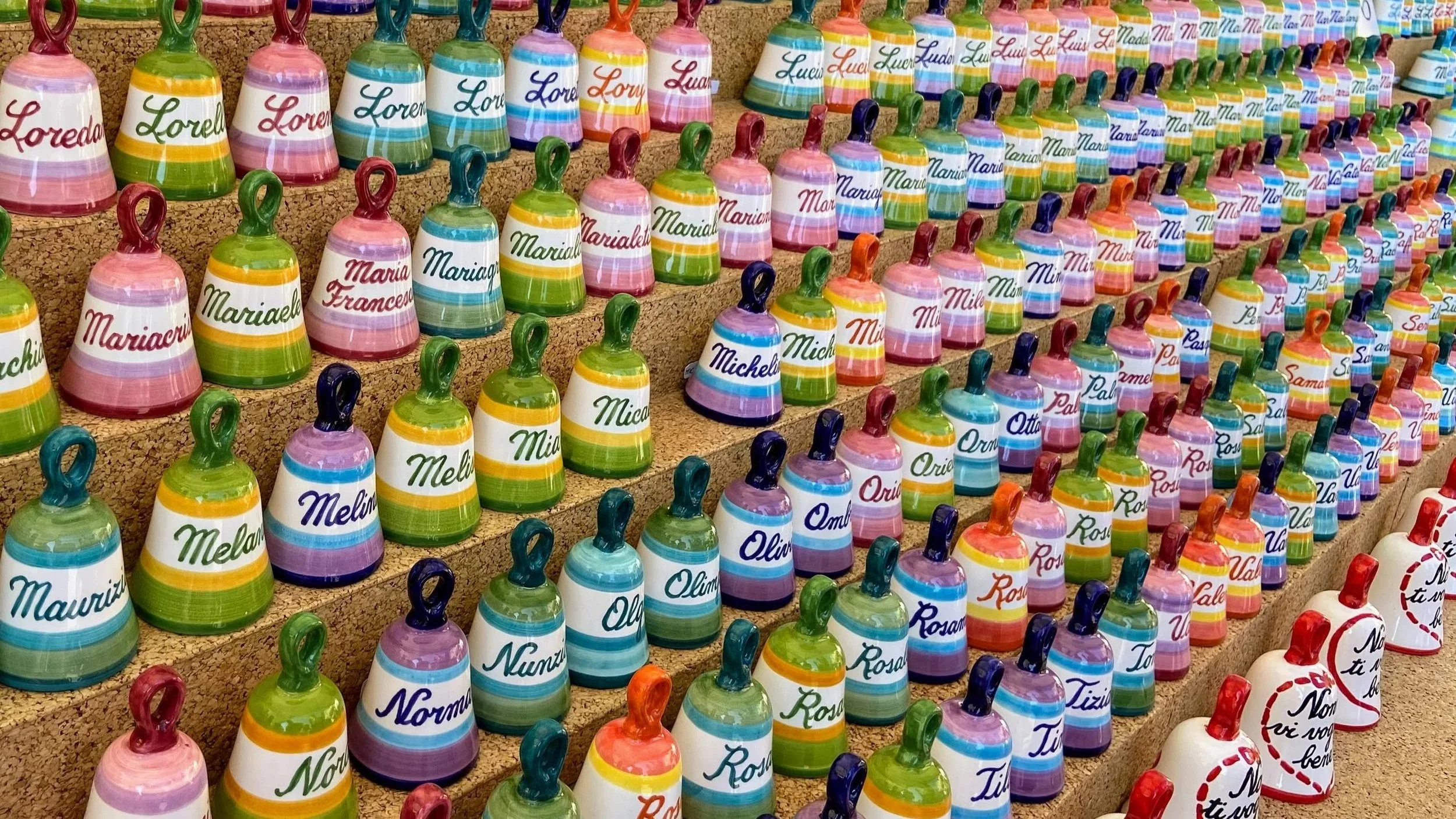 A display of colorful little ceramic bells, featuring popular first names in Italy
