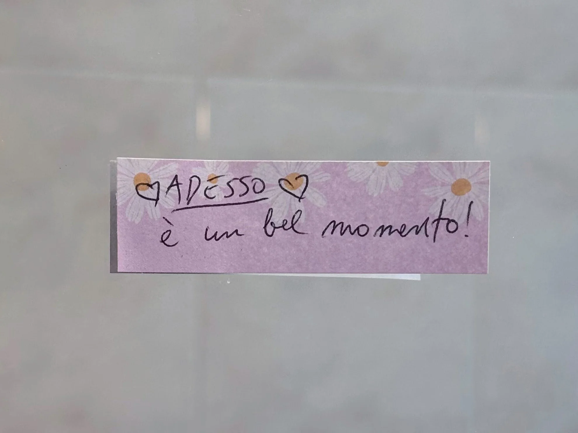 a pink note stuck on a mirror saying in Italian:  NOW is a beautiful moment!