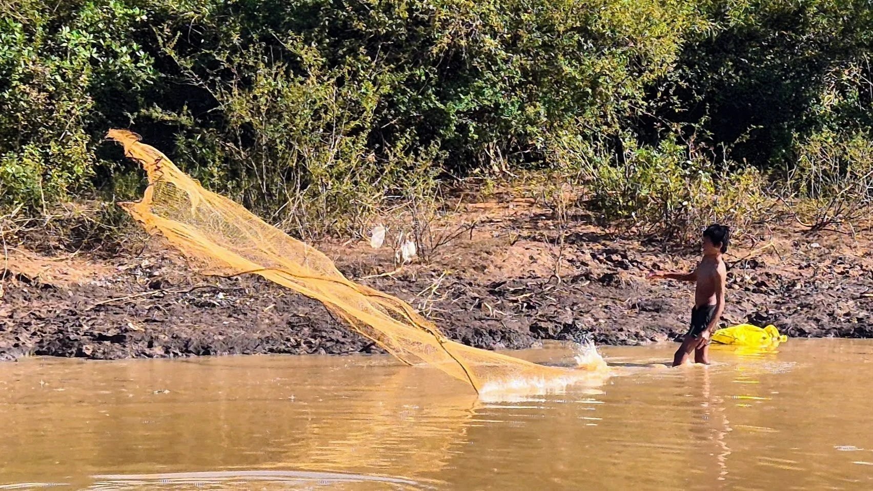 boy fishing with a net on the river in Kampong Phluk, Cambodia