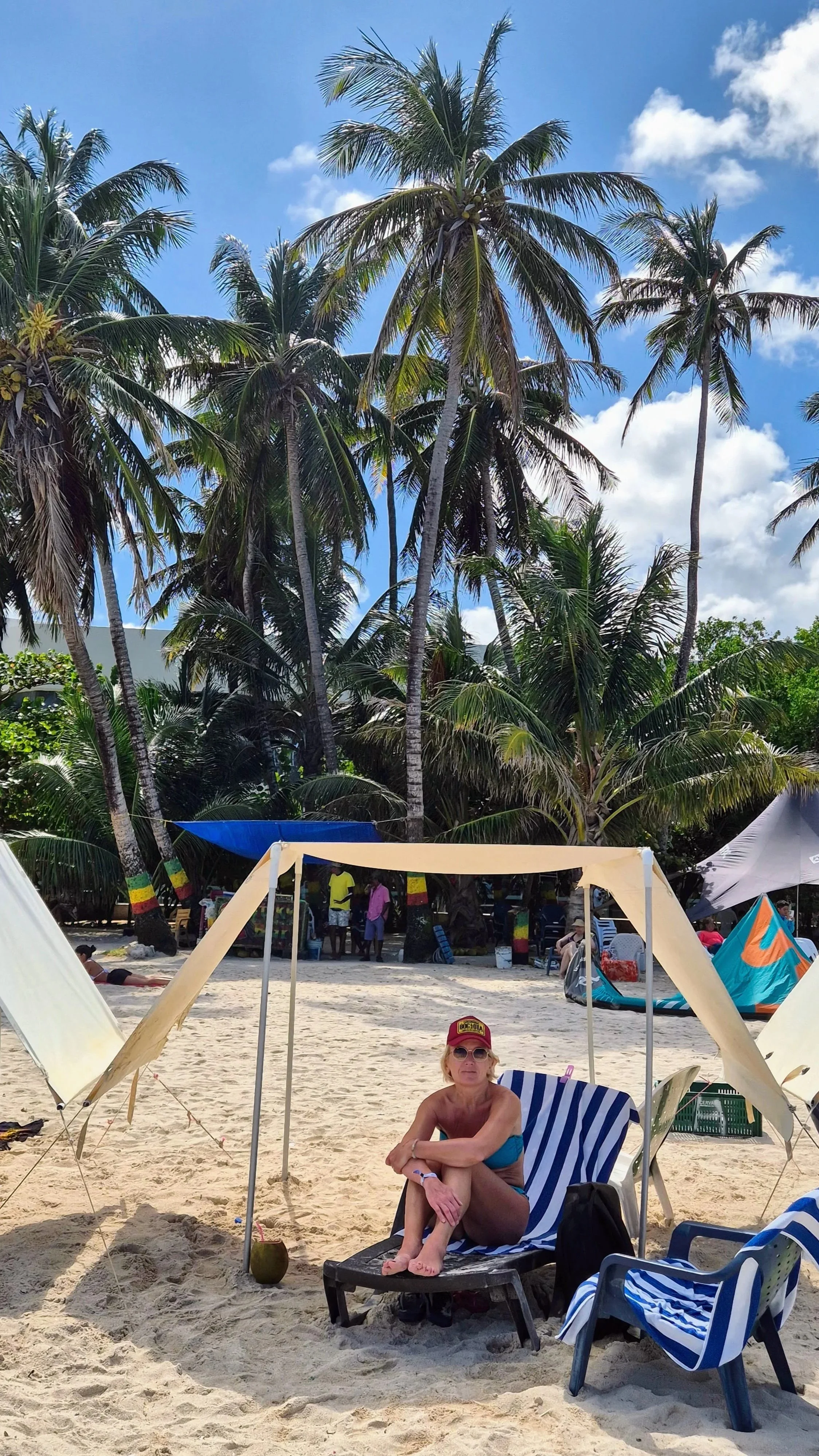 Anita under a white tent-like sun protector on a white beach in San Andres Colombia, with tall palmtrees in the background