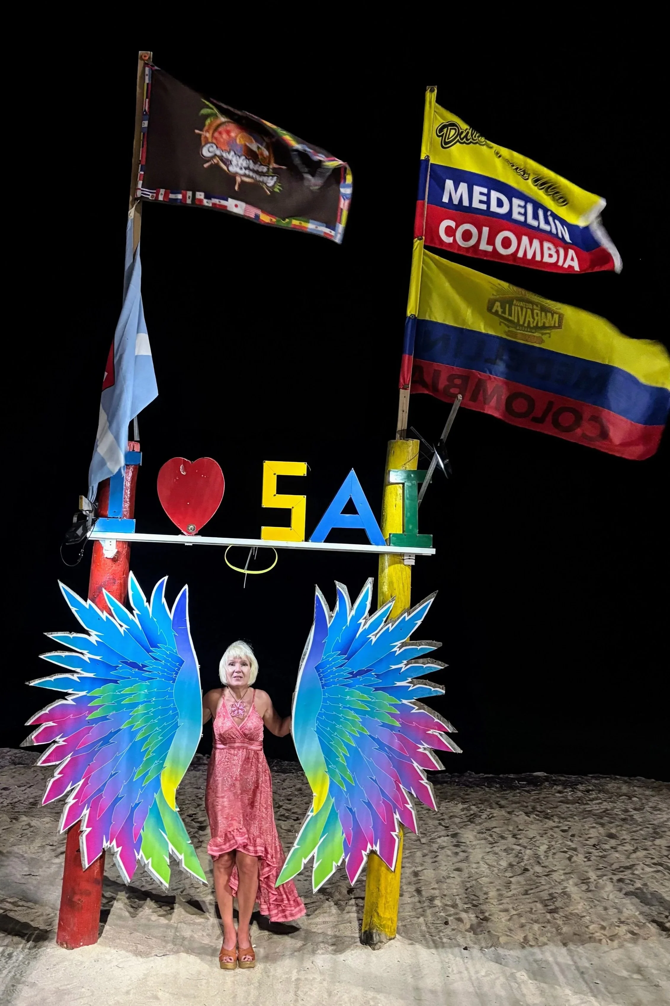 Anita with the angel wings and "I love SAI" sign and colombian city flags on the beach in san andres colombia