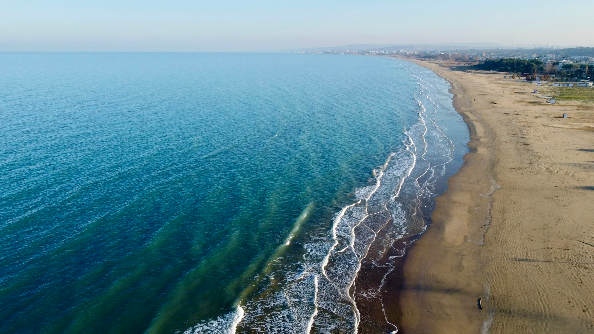 Aerial view of a sandy beach in Vasto Marina, Abruzzo, Italy, with gentle waves, alongside a coastline with structures and greenery in the background.