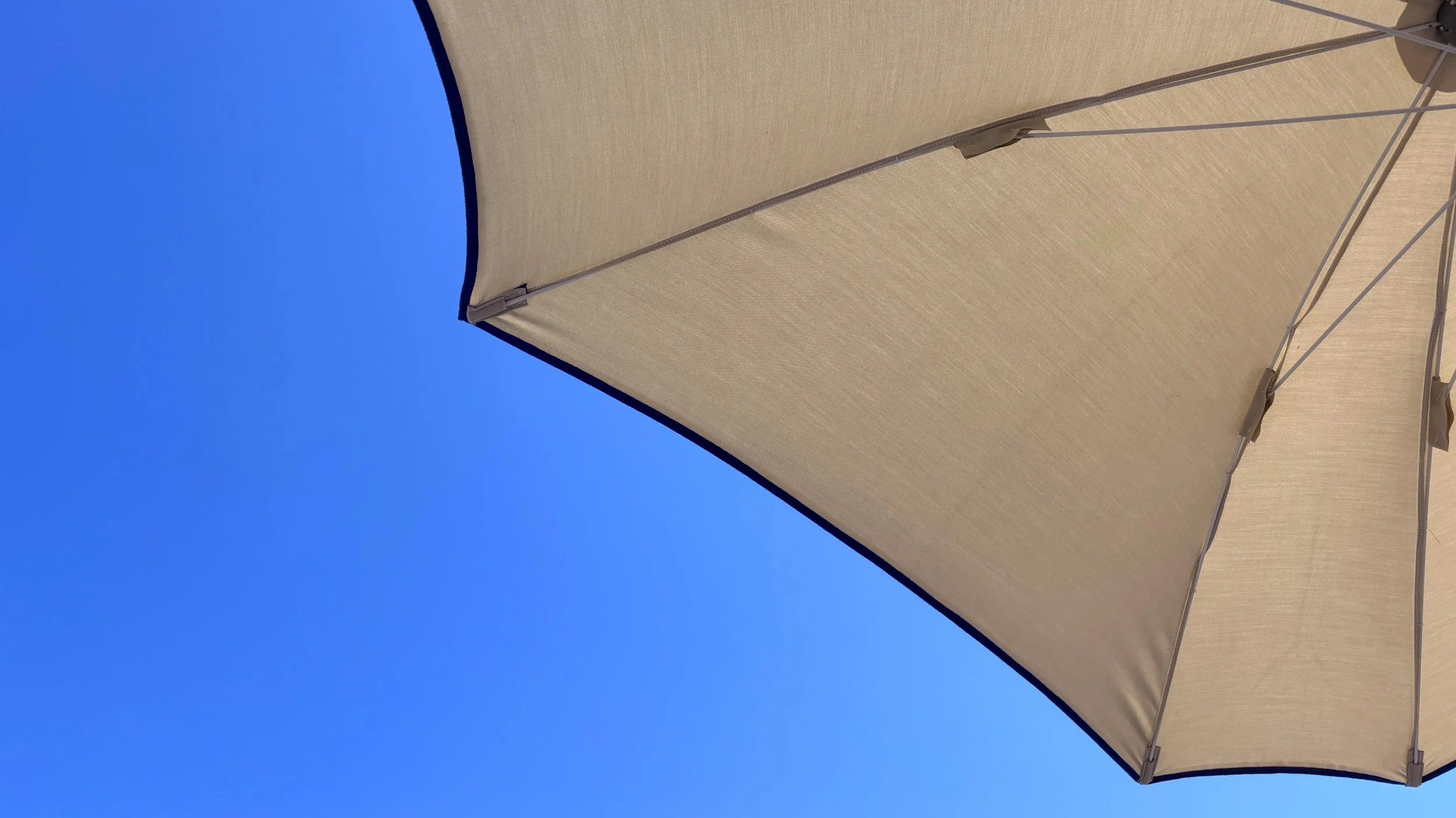 A photo of an umbrella and blue sky, taken upwards, lying on a sunbed