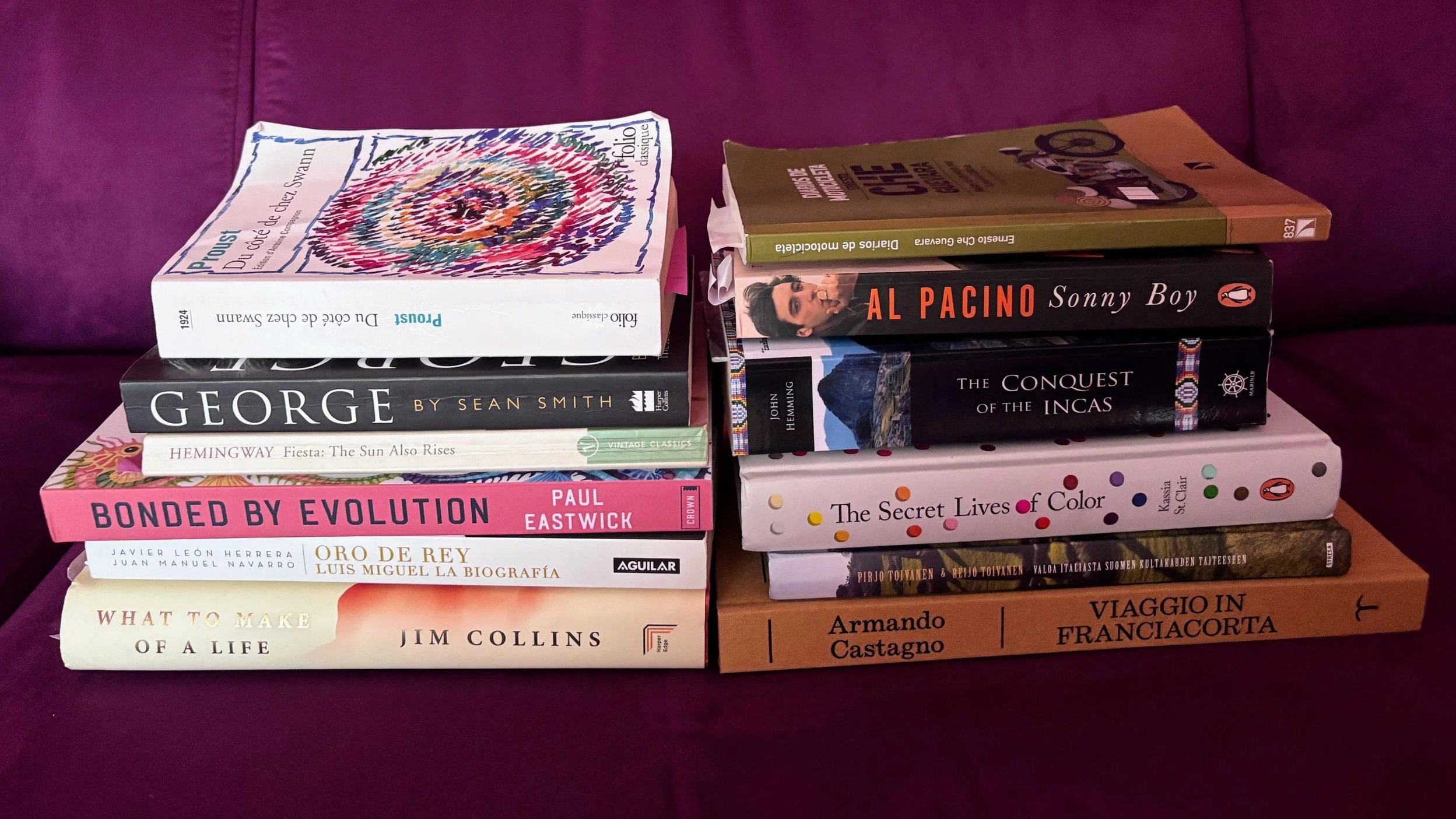 Two piles of books  on a purple sofa
