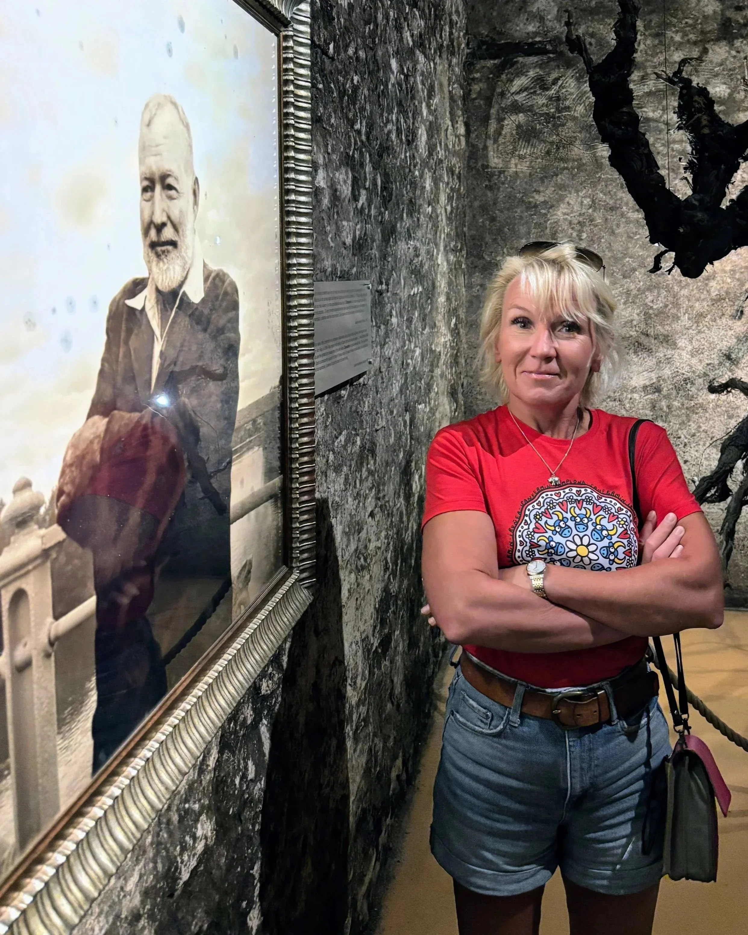 Anita standing next to a Hemingway portrait in the cellars of Bodegas Franco Espanolas in Logrono, La Rioja, Spain