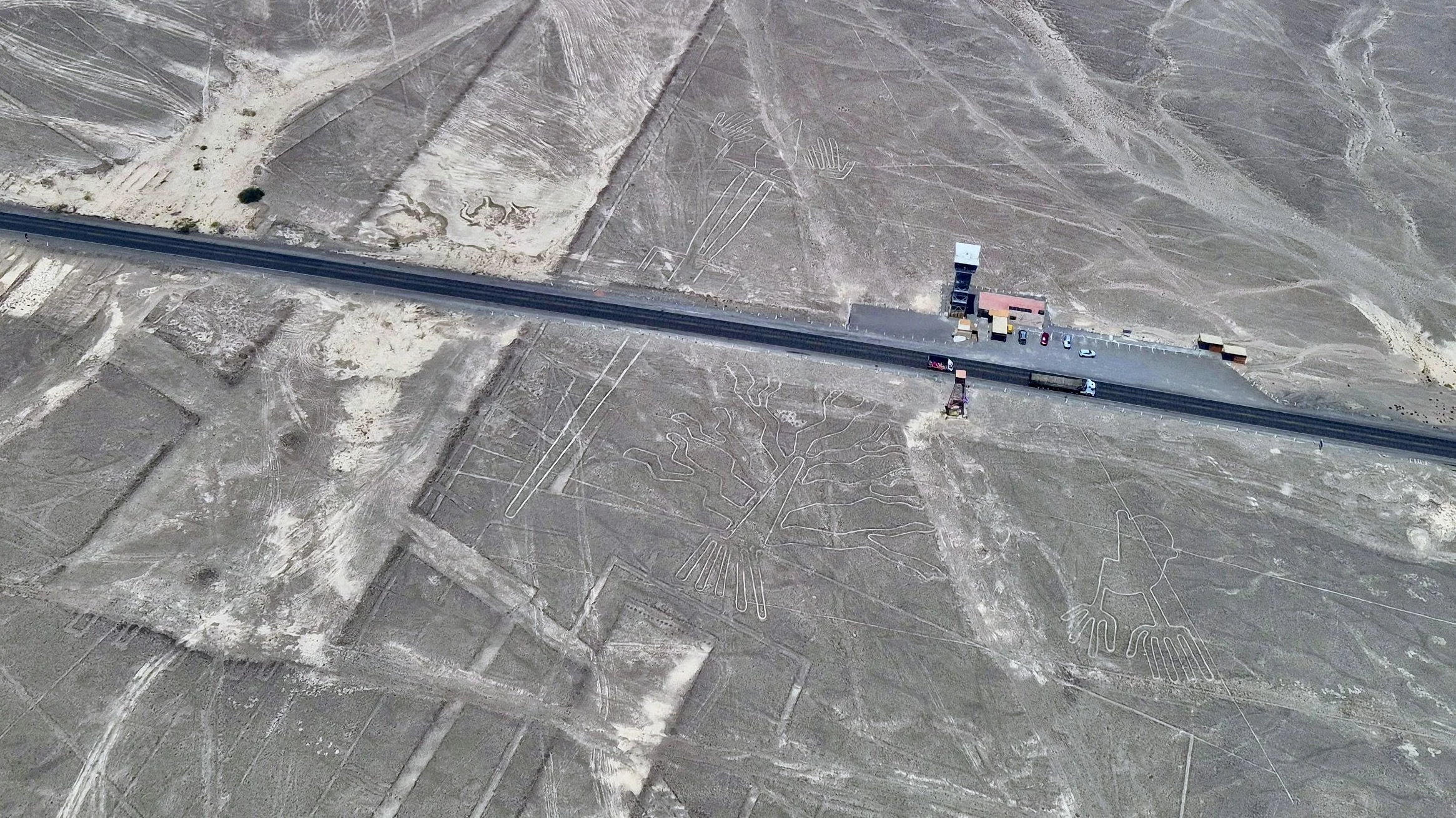 Three Nazca Lines Geoglyph, photo taken from an airplane flying above. The landscape is cut diagnally by a long straight road.