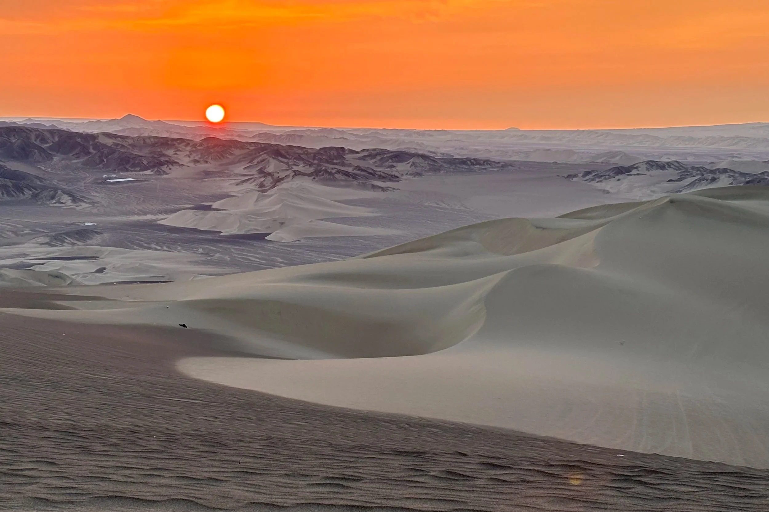 Sunset in the Ica desert in Peru, with a low sun on an orange sky and sunlight reflecting on the sand dunes