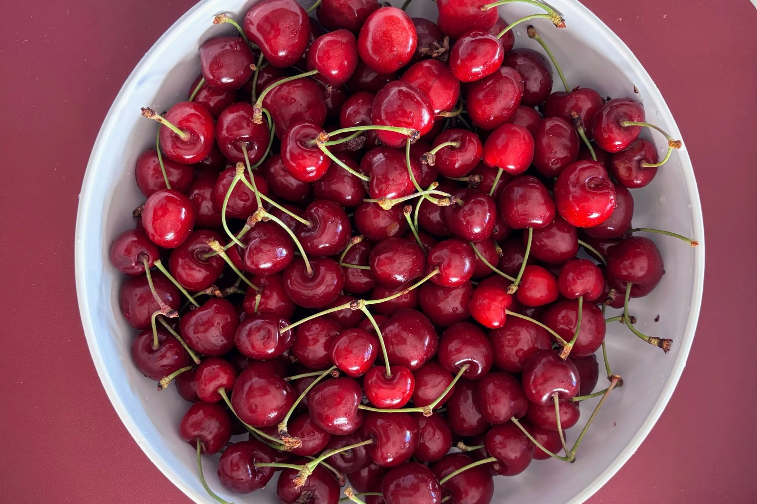 A white bowl of fresh cherries on a red surface