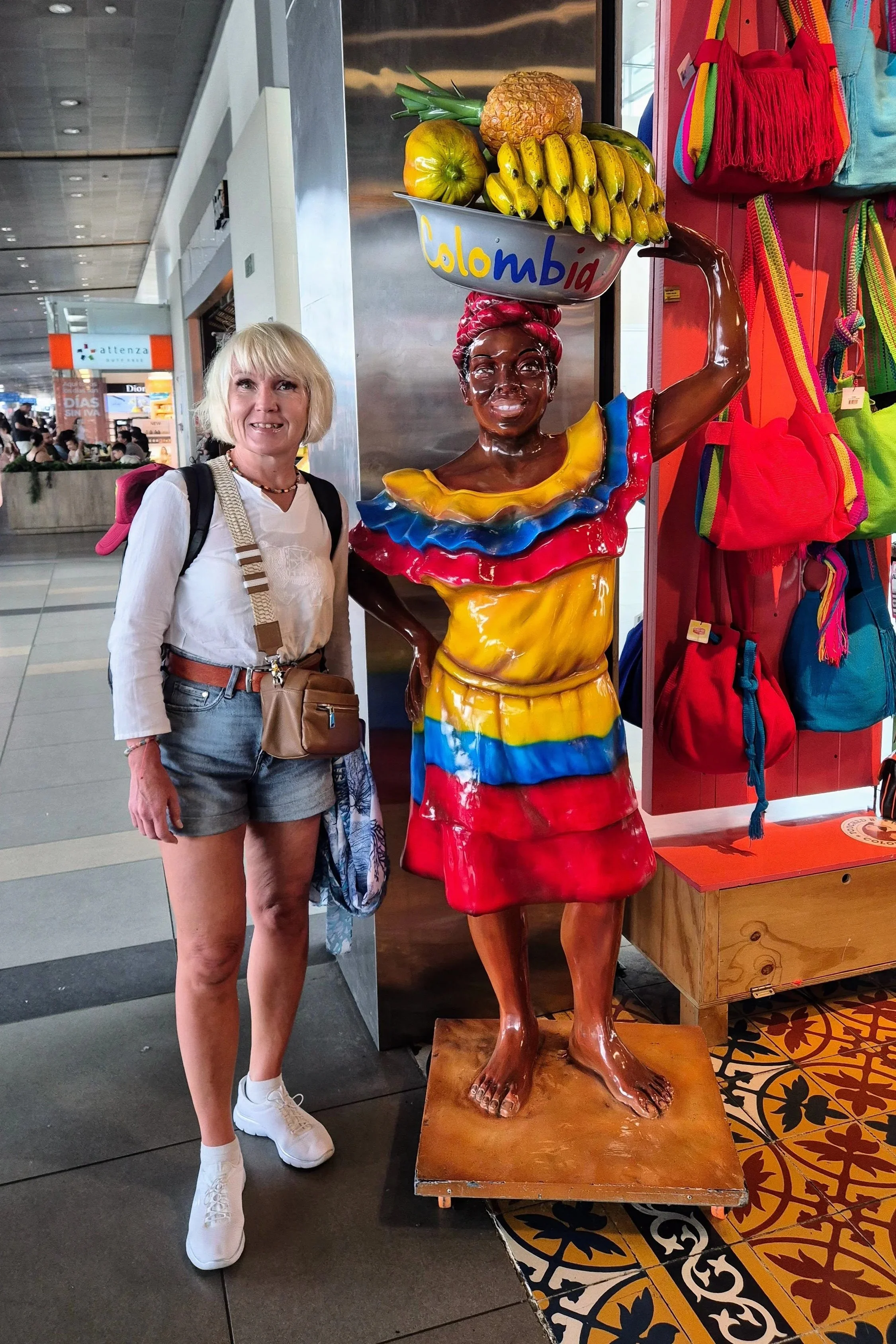 Anita next to a statue of black lady wearing a dress with Colombia's national colors and carrying a bowl of tropical fruit on her head
