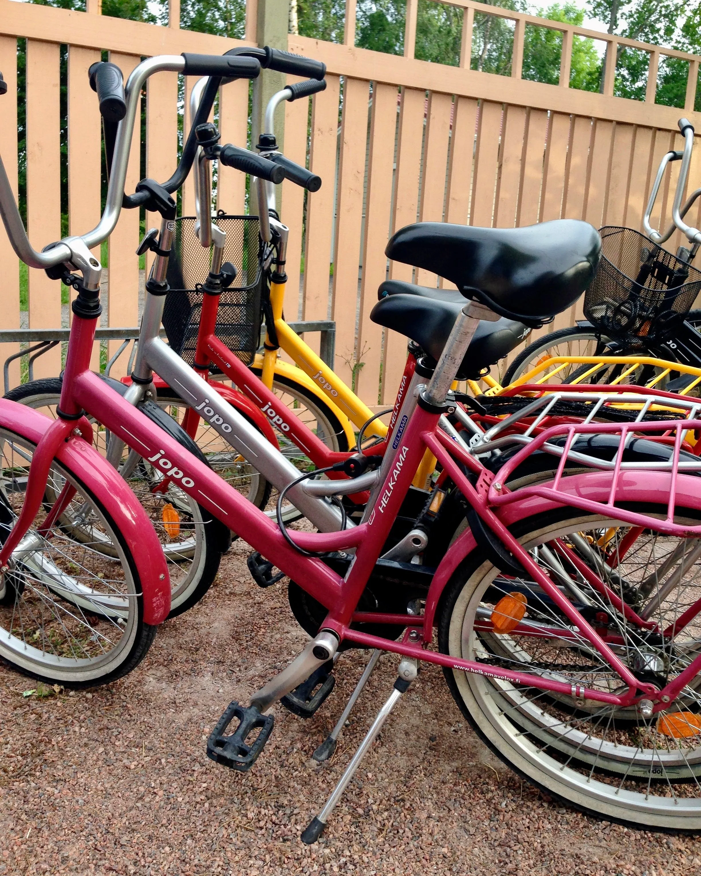 Four colorful Jopo-branded bikes parked in front of a wooden fence in Hanko, Finland