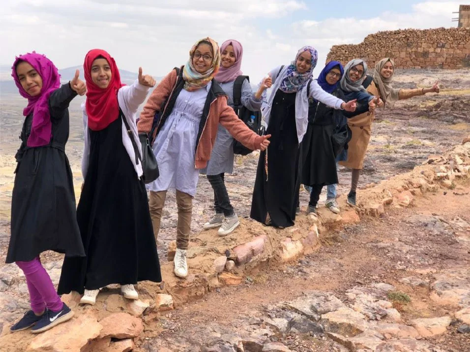 A group of young girls stand on the base of an agricultural wall while giving 'thumbs up' gesture 