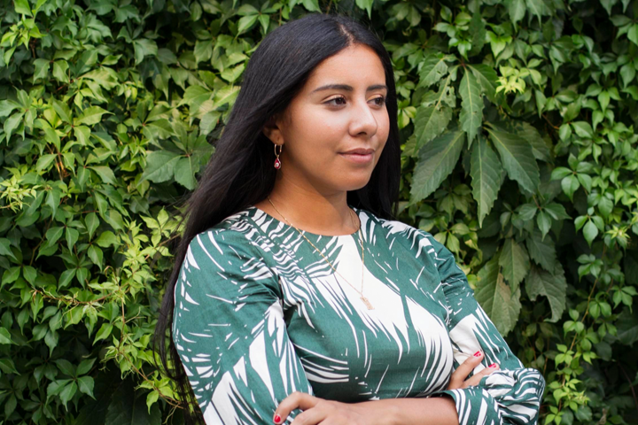A profile of Ayat Mneina standing in front of a wall of leaves