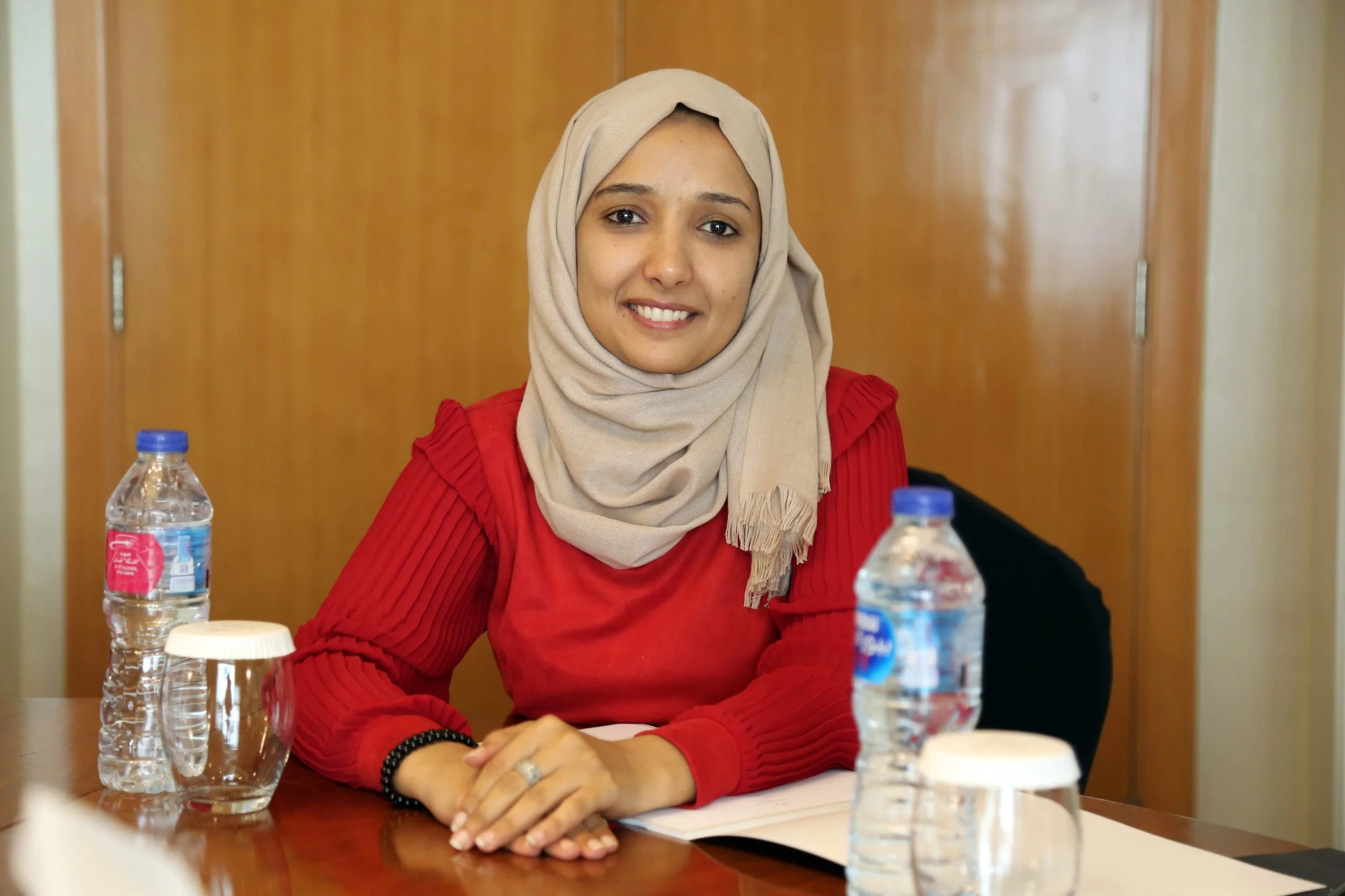 A profile photograph of Ola Al-Aghbary, smiling at the camera while sat at a table