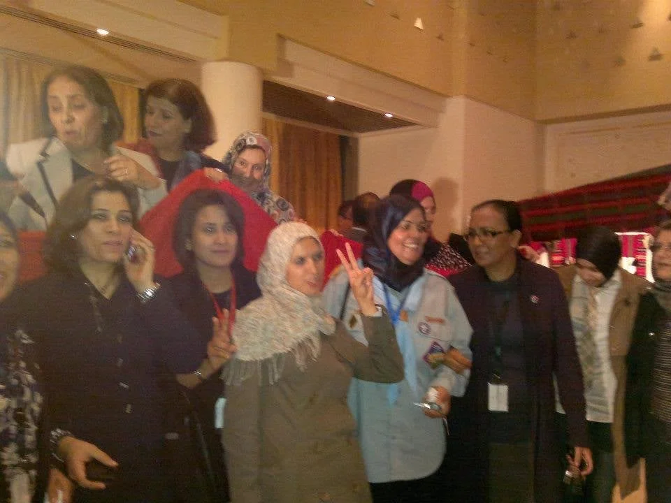 A large gathering of women posing for photos in two rows. The second row of women hold a large Libyan flag of the design reintroduced by the transitional council as the national flag