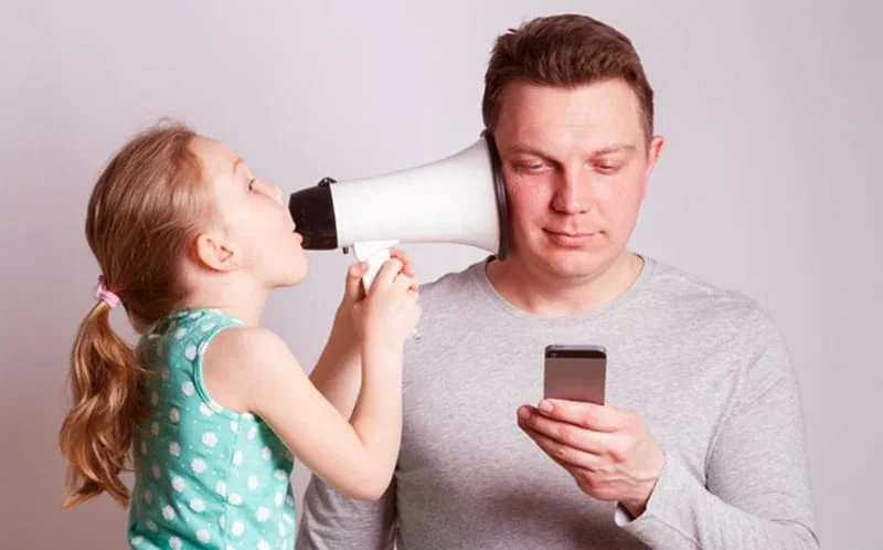 image of a man on his cell phone while a young girl points a megaphone into his ear