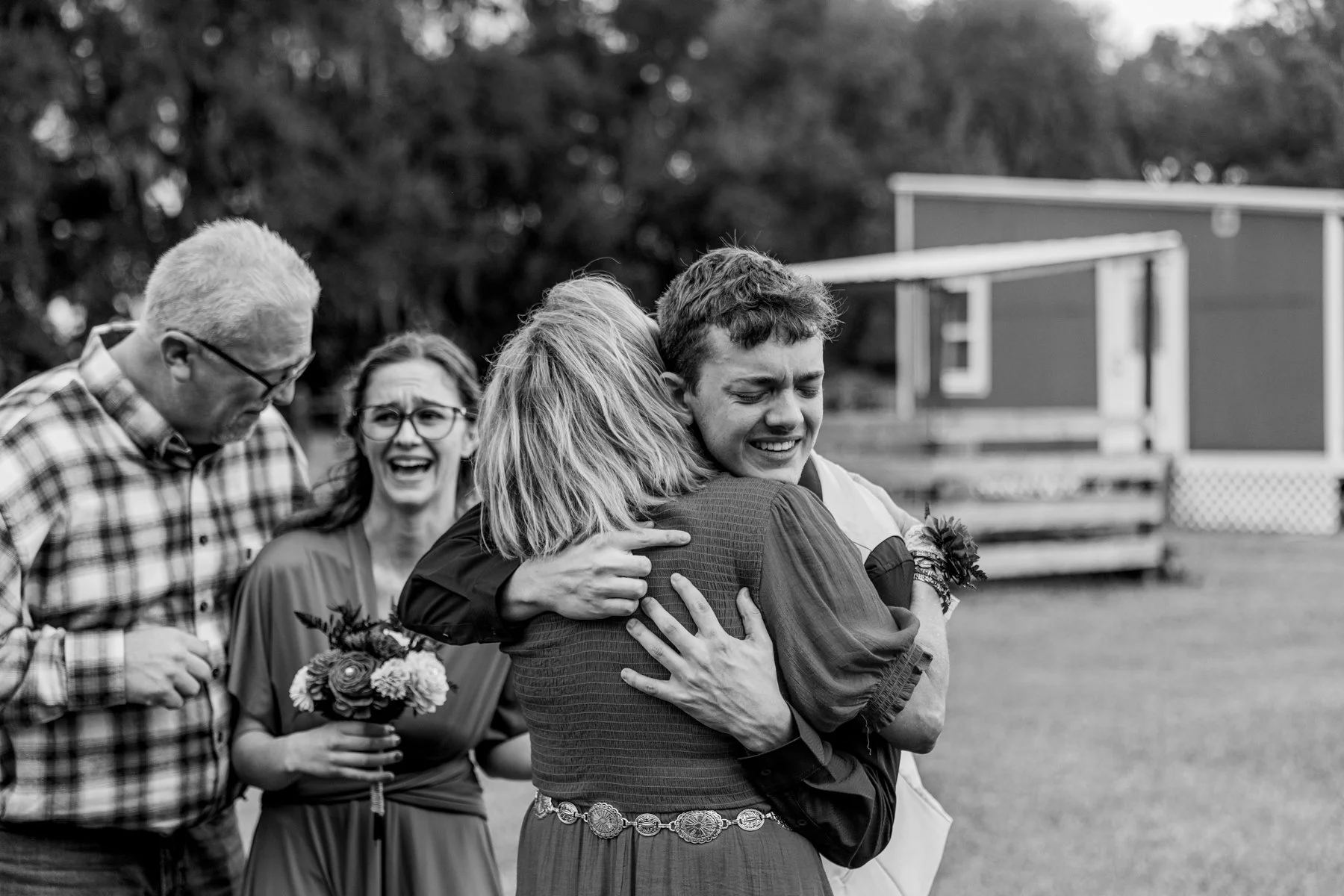 After the ceremony, the groomsman hugs the grooms mother while in the background a bridesmaid lets go of some nervous teary laughter.