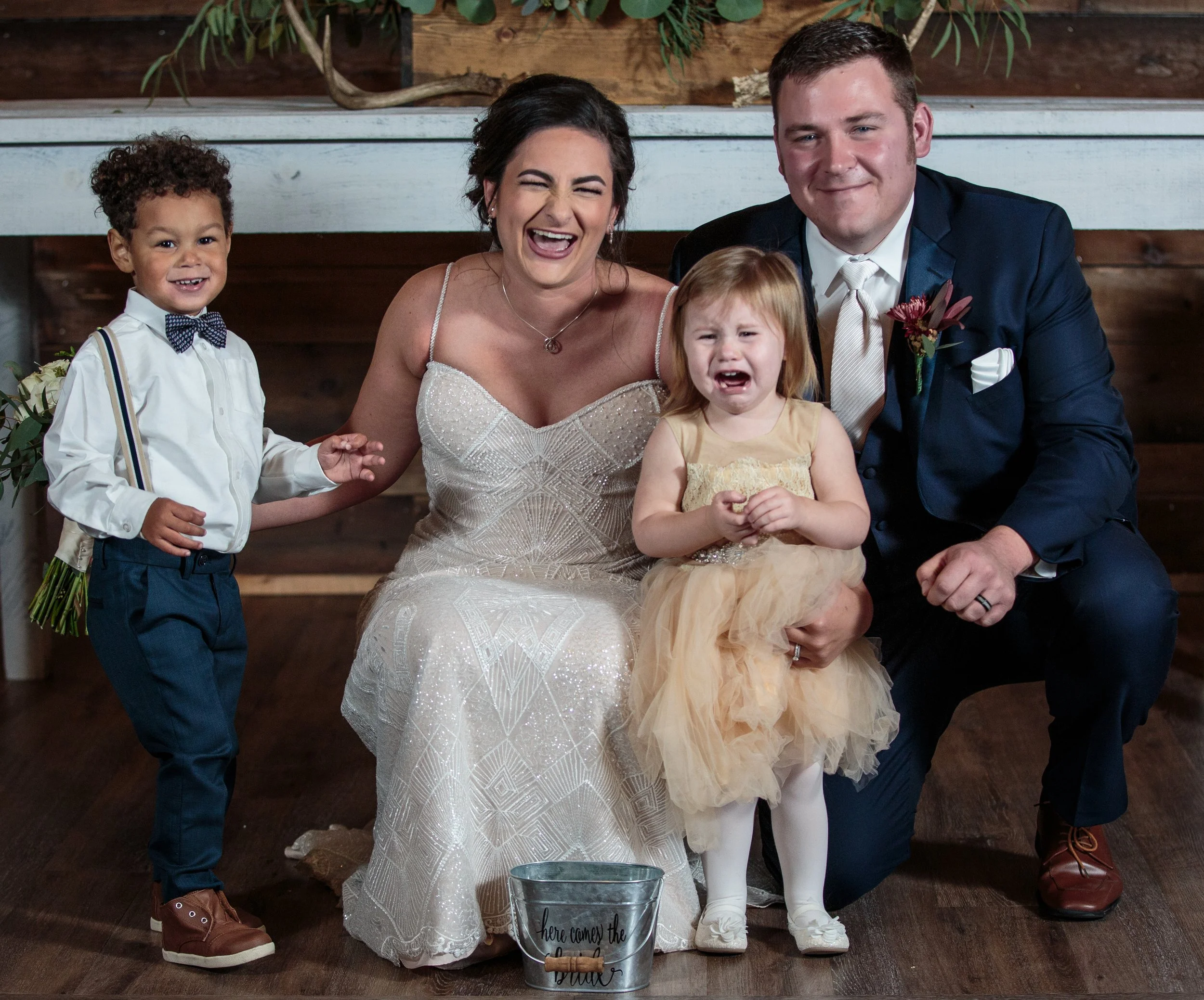 Bride and groom posing with young children, candid family photo with smiling and crying child during wedding