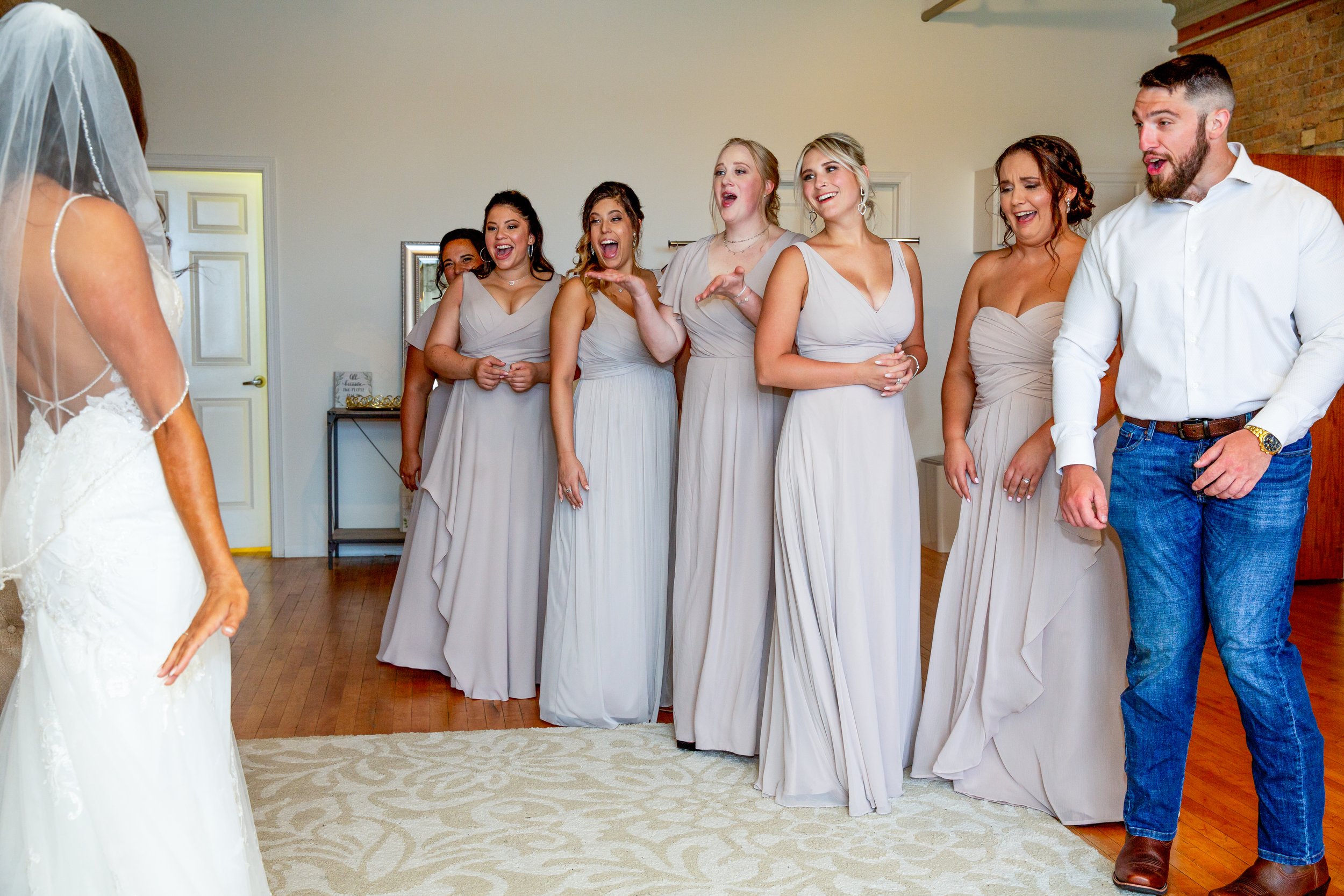 The bridesmaids of the bride turn to see her in her wedding dress for the first time. They all show looks of surprise.