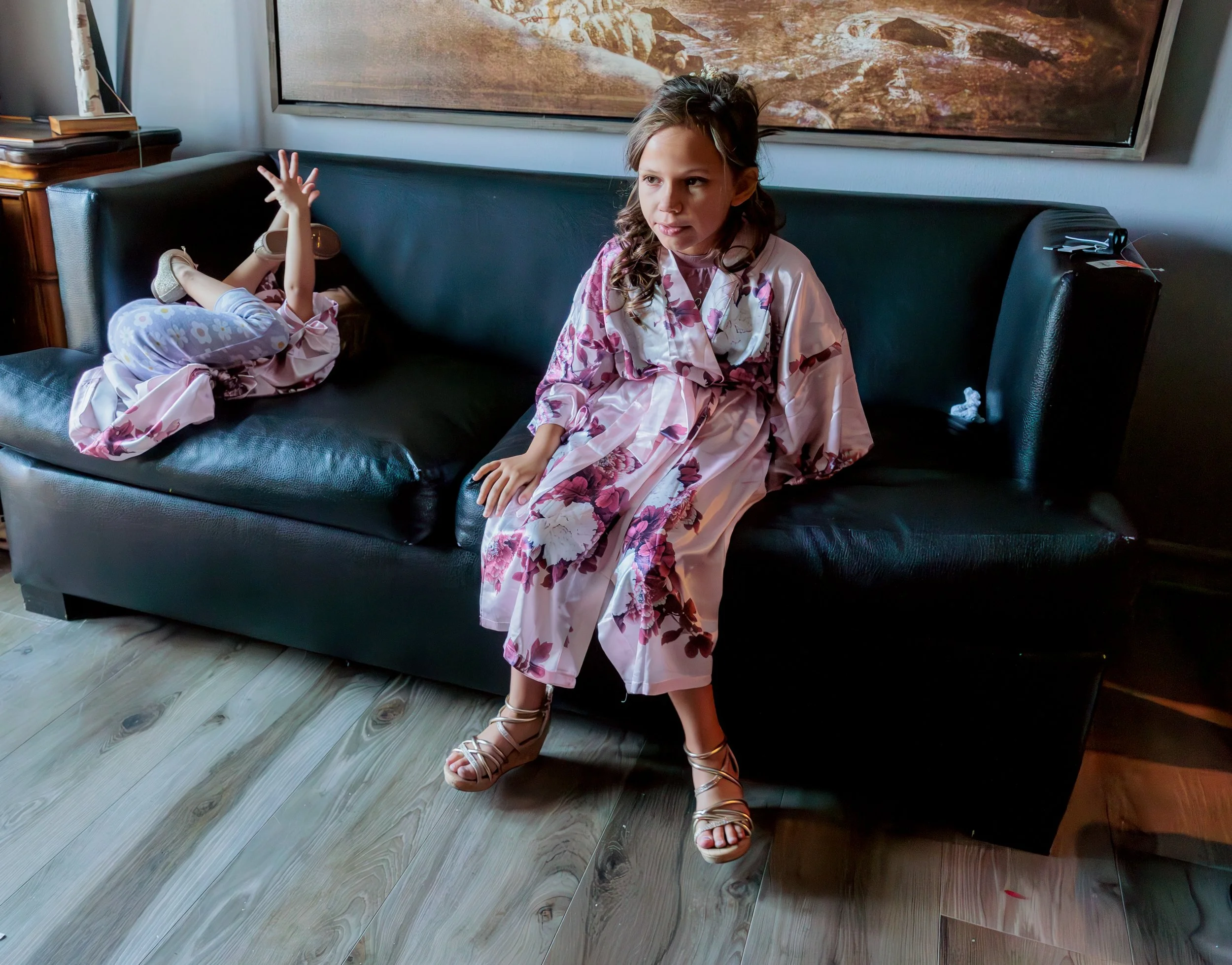 Young girls in floral robes sitting on couch while getting ready for wedding, candid pre-ceremony moment with children