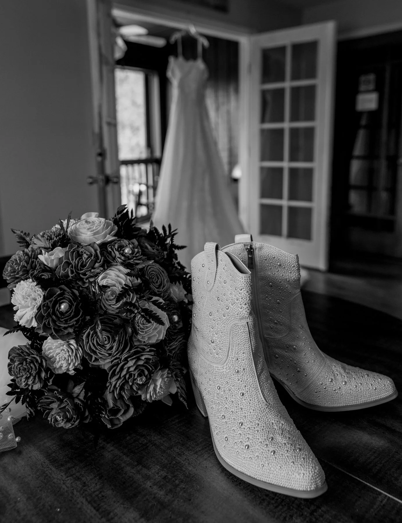 Wedding dress hanging in background of white wedding cowboy boots.