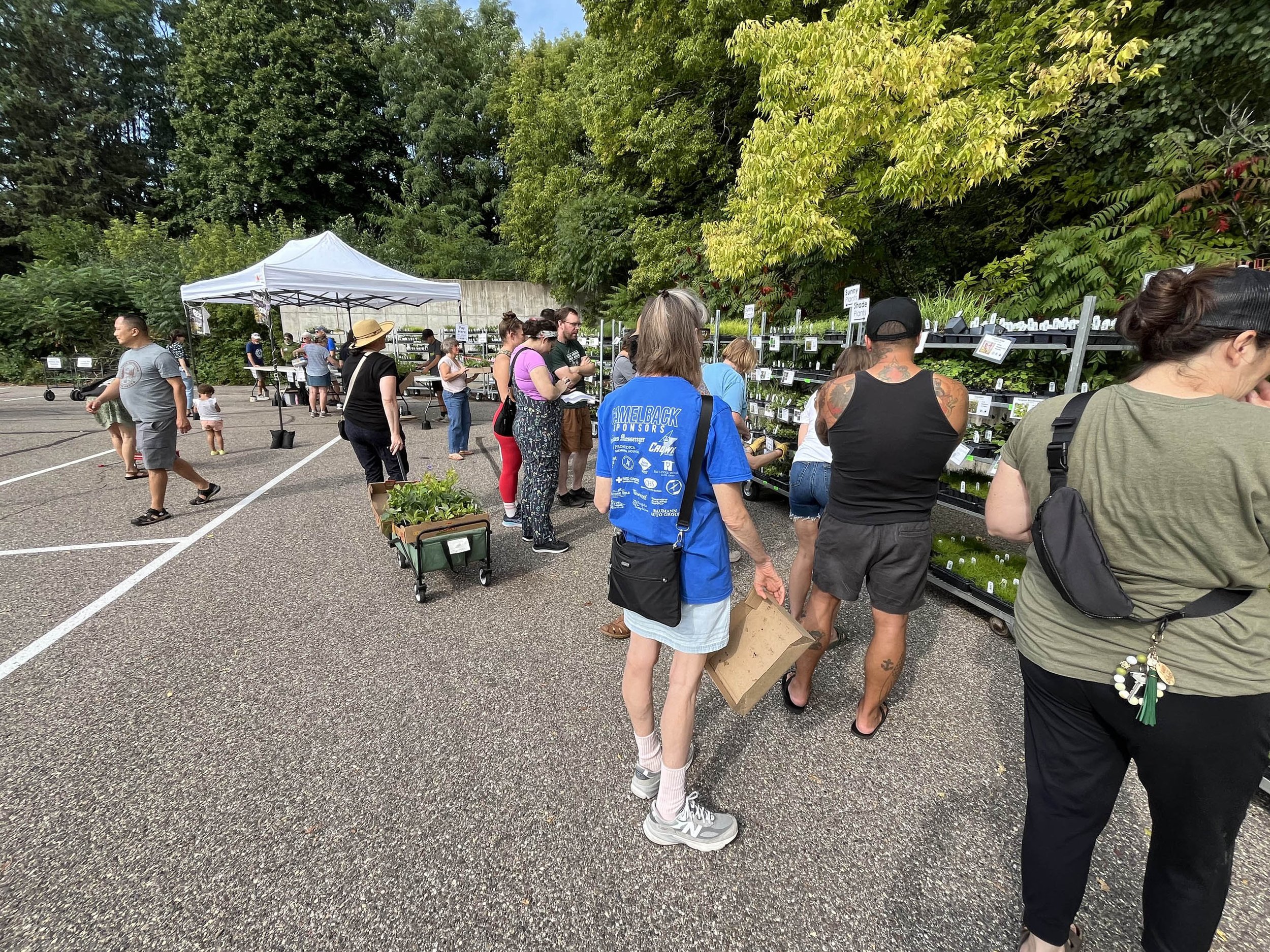 People standing next to metal plant sales rack with plants waiting to buy native plants