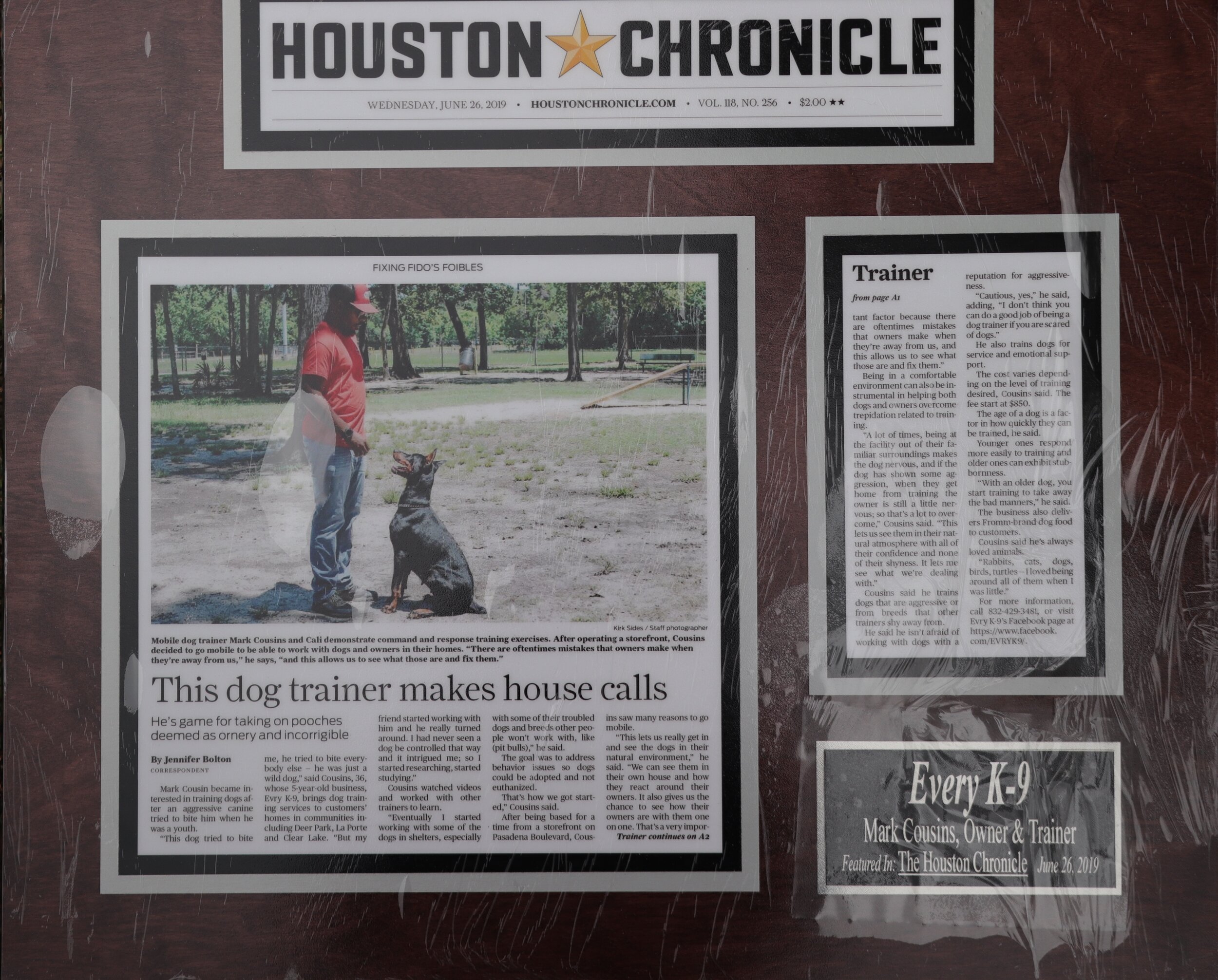 Framed newspaper article about a dog trainer, featuring a photo of a man training a dog outdoors from the Houston Chronicle dated June 26, 2019.