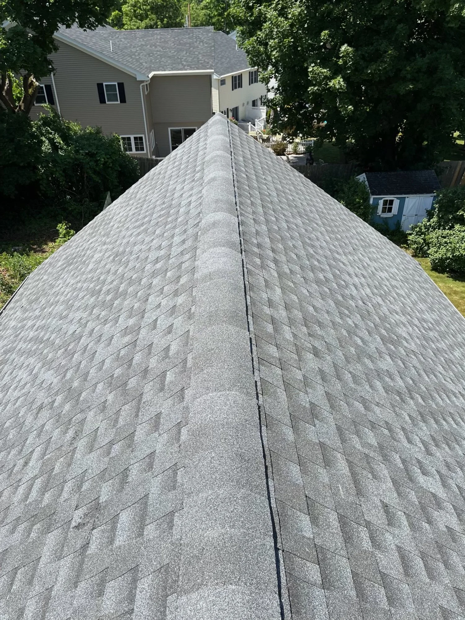 Looking down a roof with gray shingles, with neighboring houses and trees in the background.